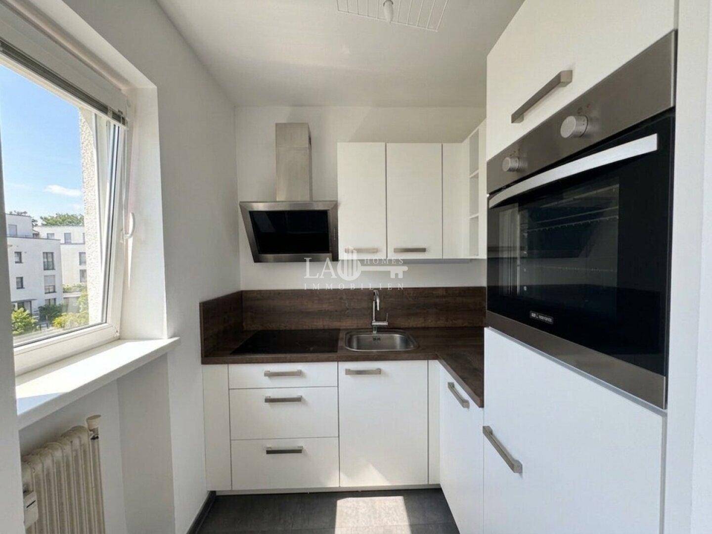 Moderne, kompakte Küche mit weißen Schränken, Einbauofen und Fenster.