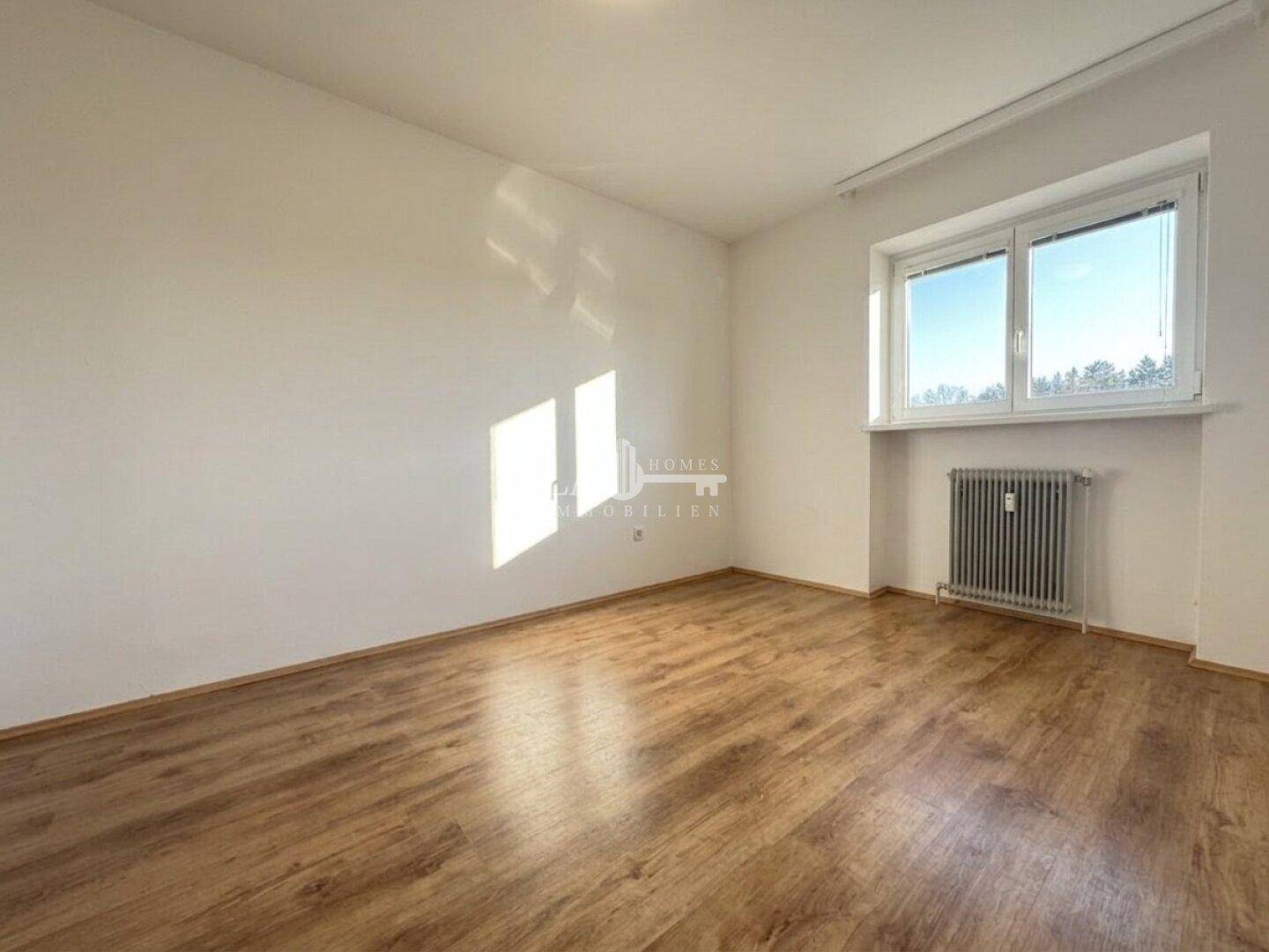 Leerer Raum mit Holzfußboden, Fenster, Heizkörper und viel Tageslicht.