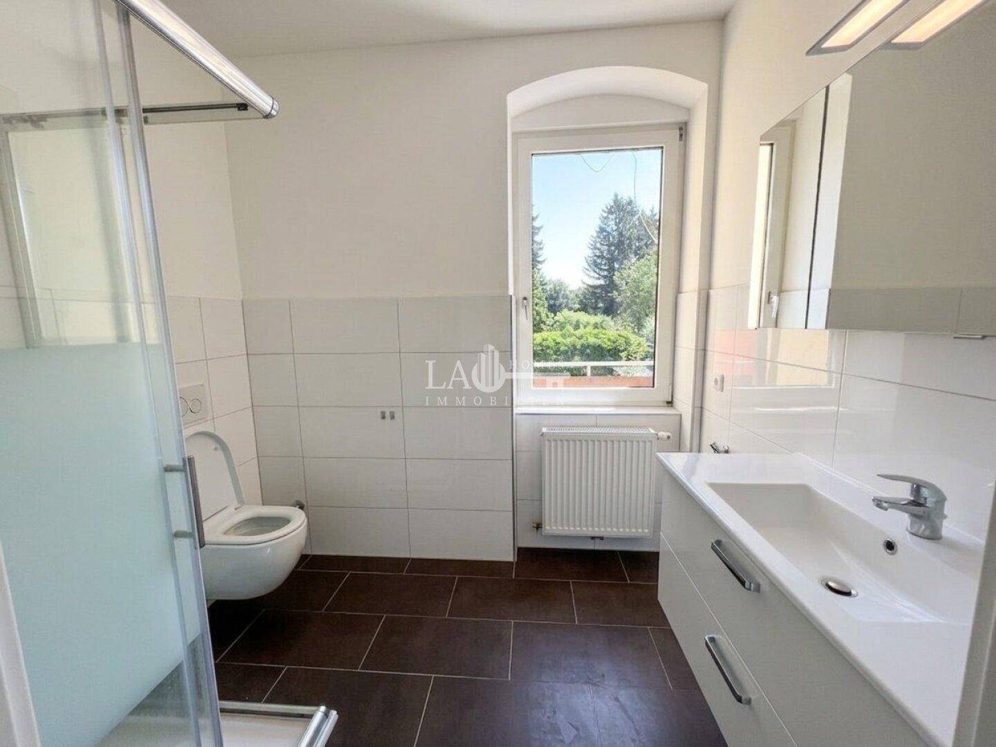 Helles Badezimmer mit Fenster, Duschkabine, WC und modernem Waschtisch, ausgestattet mit weißen und braunen Fliesen.