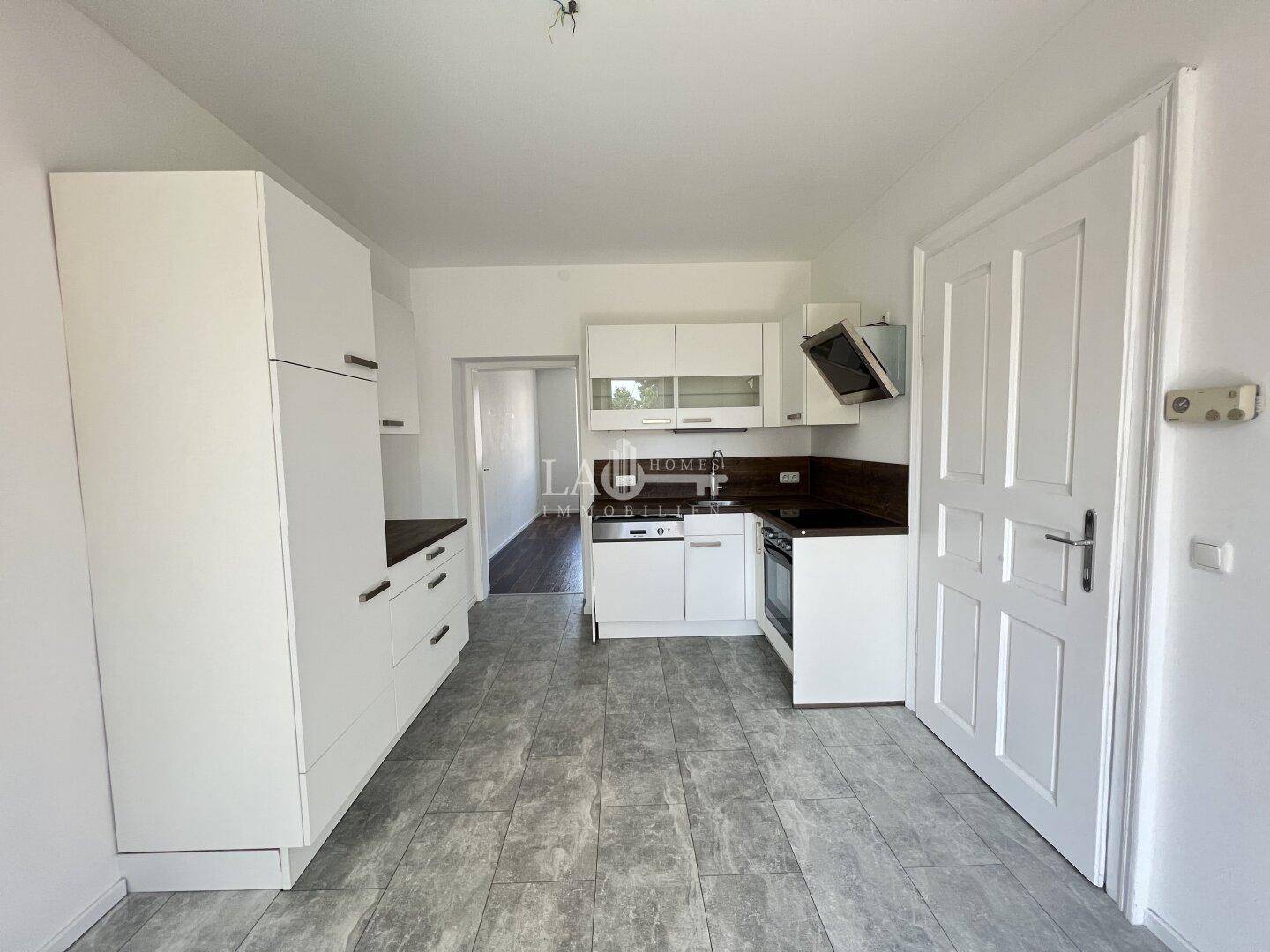 Funktionale Küche mit weißen Schränken, dunklen Arbeitsplatten, Backofen, Geschirrspüler und Dunstabzugshaube.
