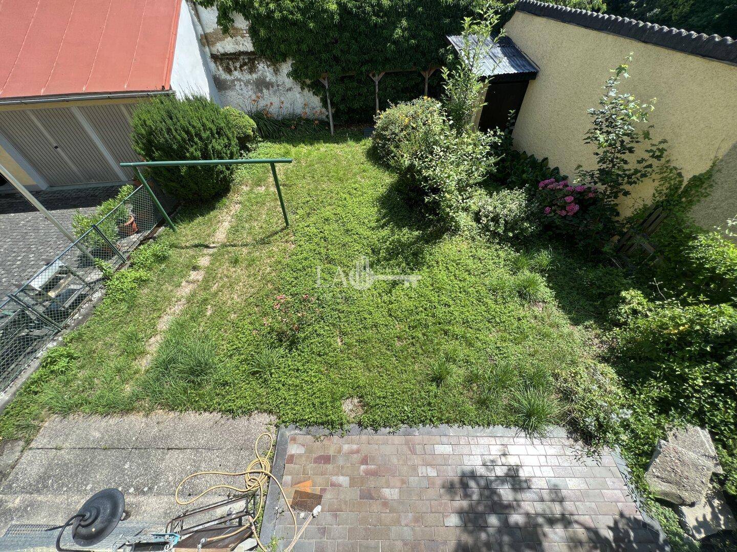 Blick von oben auf einen grünen Gartenbereich mit Rasenfläche und einigen gepflasterten Abschnitten.