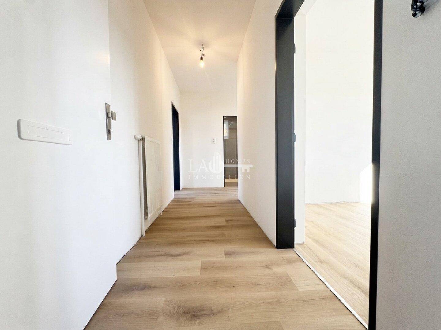 Langer, heller Flur mit modernem Laminatboden und weißen Wänden, der zu weiteren Räumen führt.