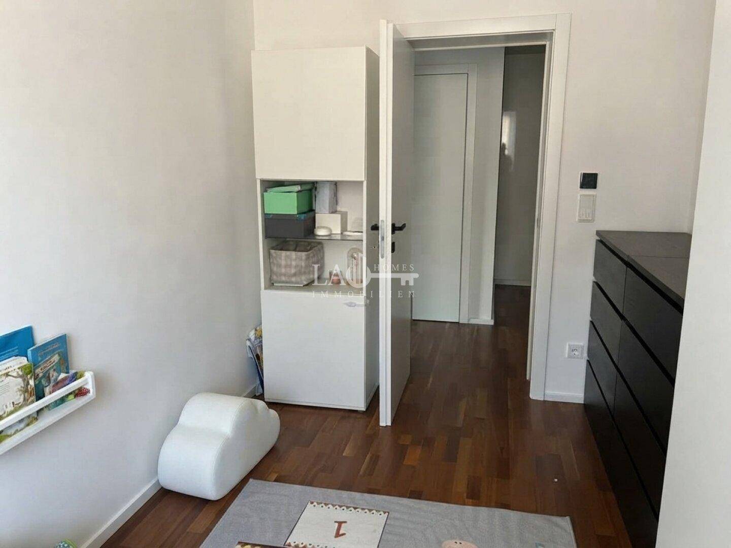 Helles Schlafzimmer mit Holzboden und schlichten weißen Möbeln, ideal als Kinderzimmer oder Gästezimmer.