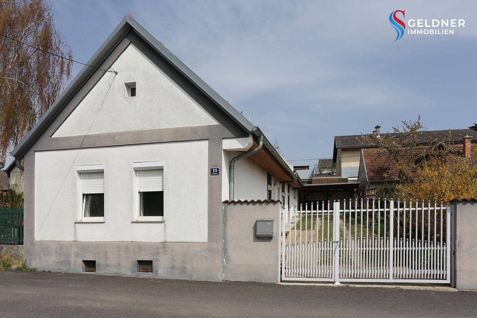Ansicht des Hauses von vorne mit weißer Fassade, Satteldach und Einfahrtstor.