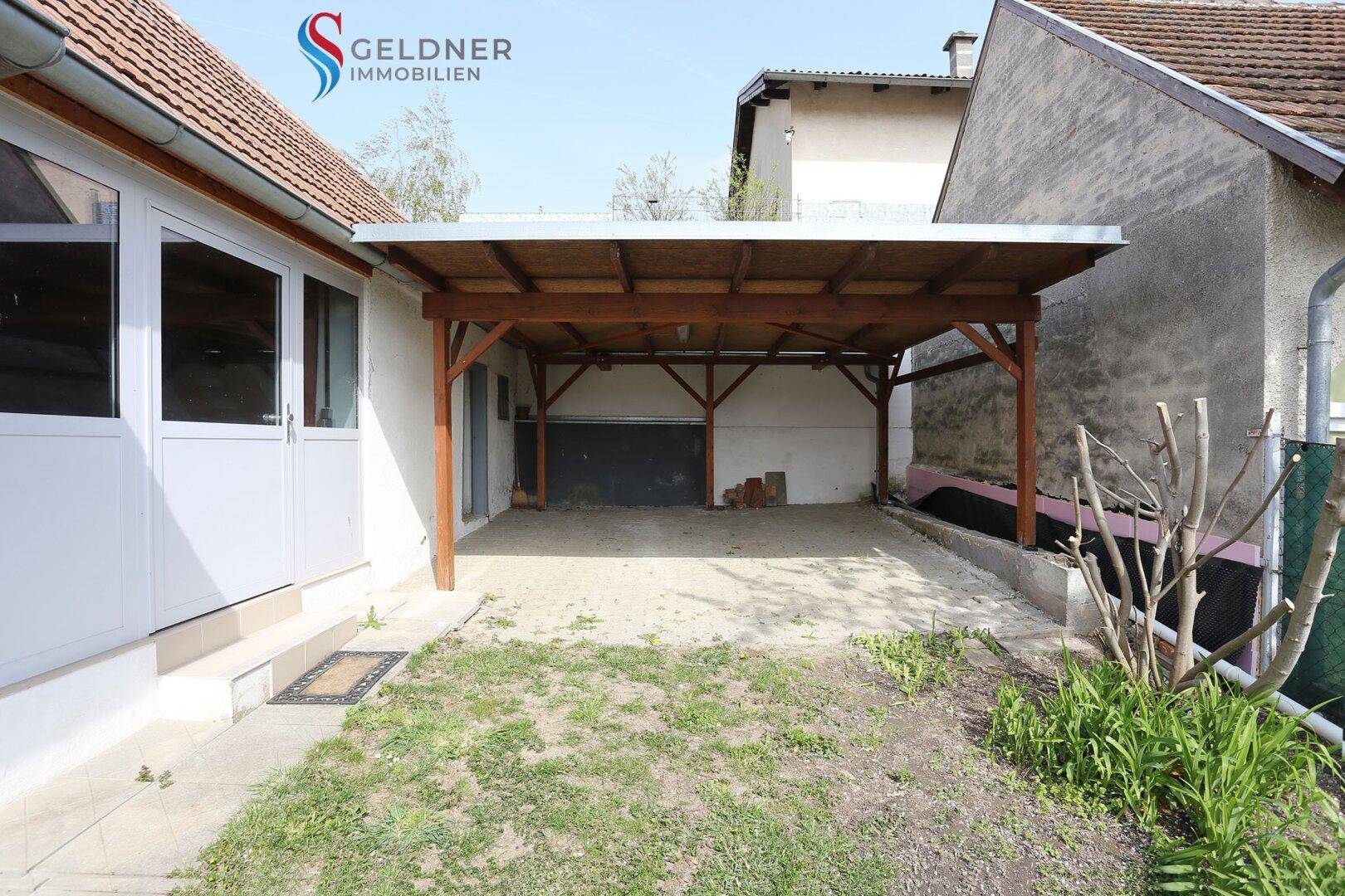 Blick auf den Carport und die gepflasterte Fläche im hinteren Bereich des Grundstücks.