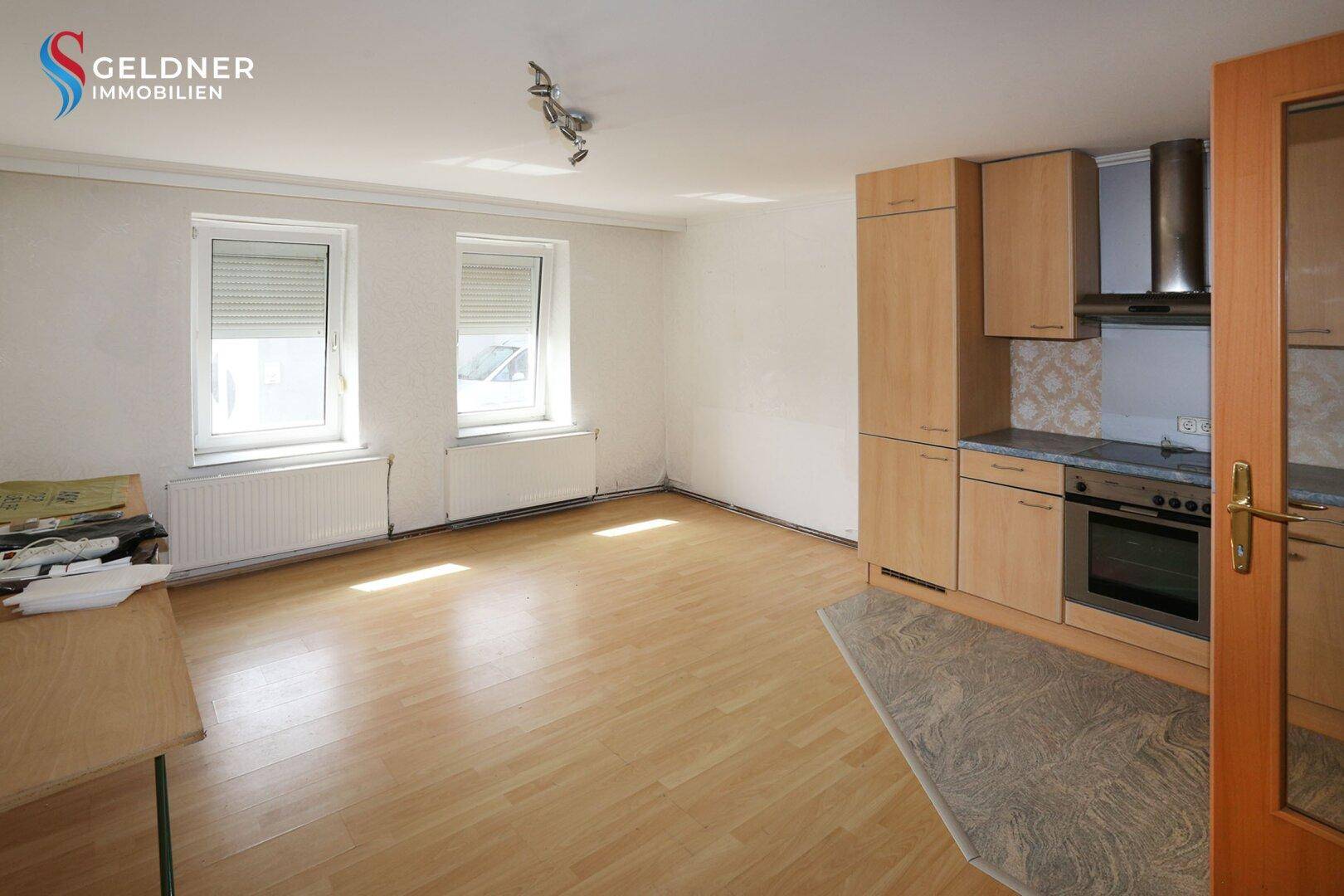 Heller Wohnbereich mit integrierter Küche, Laminatboden und Fenstern mit Rollläden.