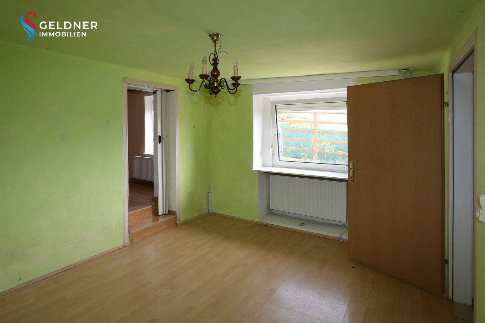 Raum mit hellgrünen Wänden, Laminatboden und einem Fenster mit Blick ins Grüne.