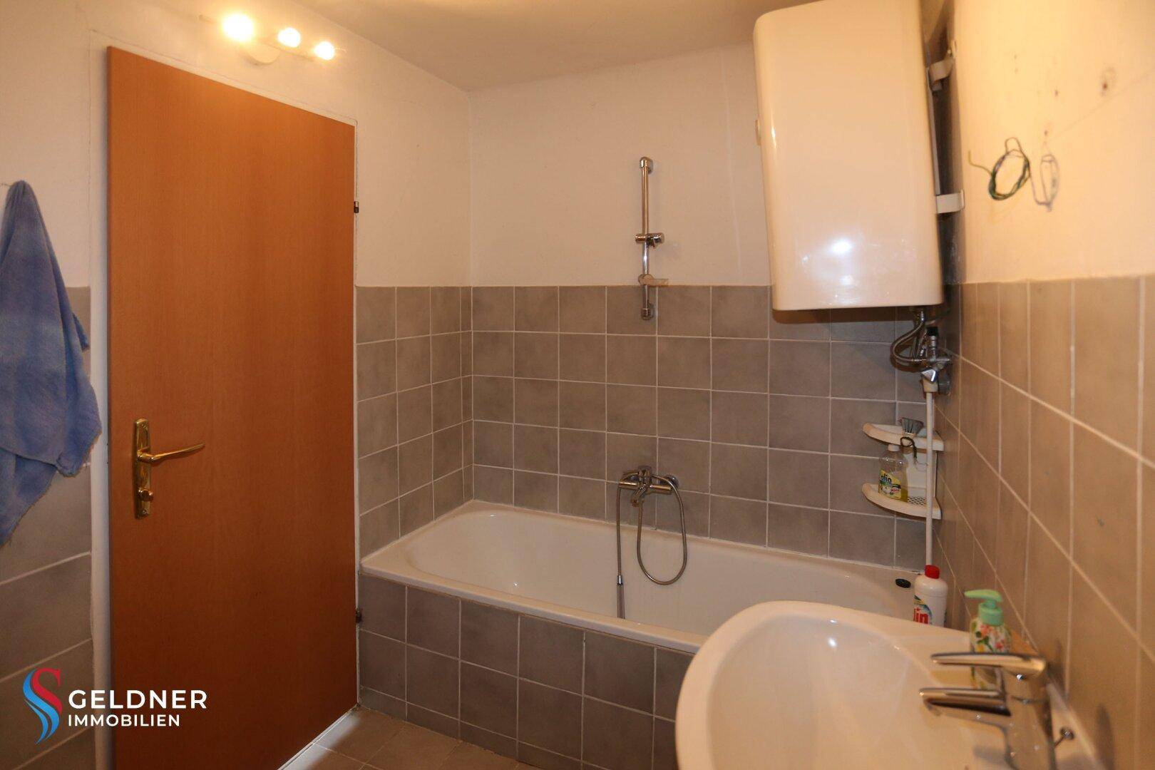 Badezimmer mit Badewanne, Waschbecken und grauen Fliesen an Wänden und Boden.