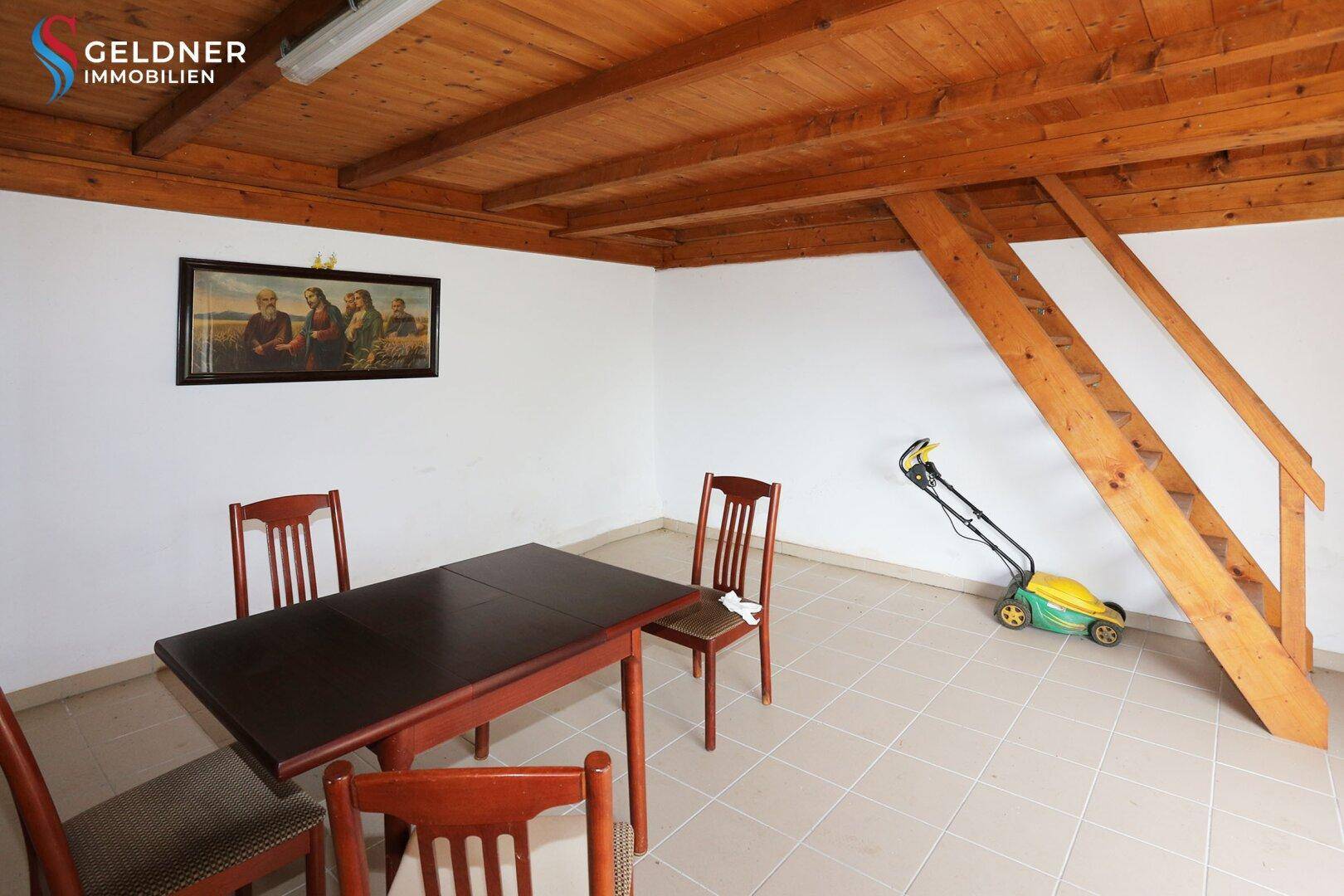 Essbereich mit Holztisch, Stühlen, Fliesenboden und einer Holztreppe zum Obergeschoss.