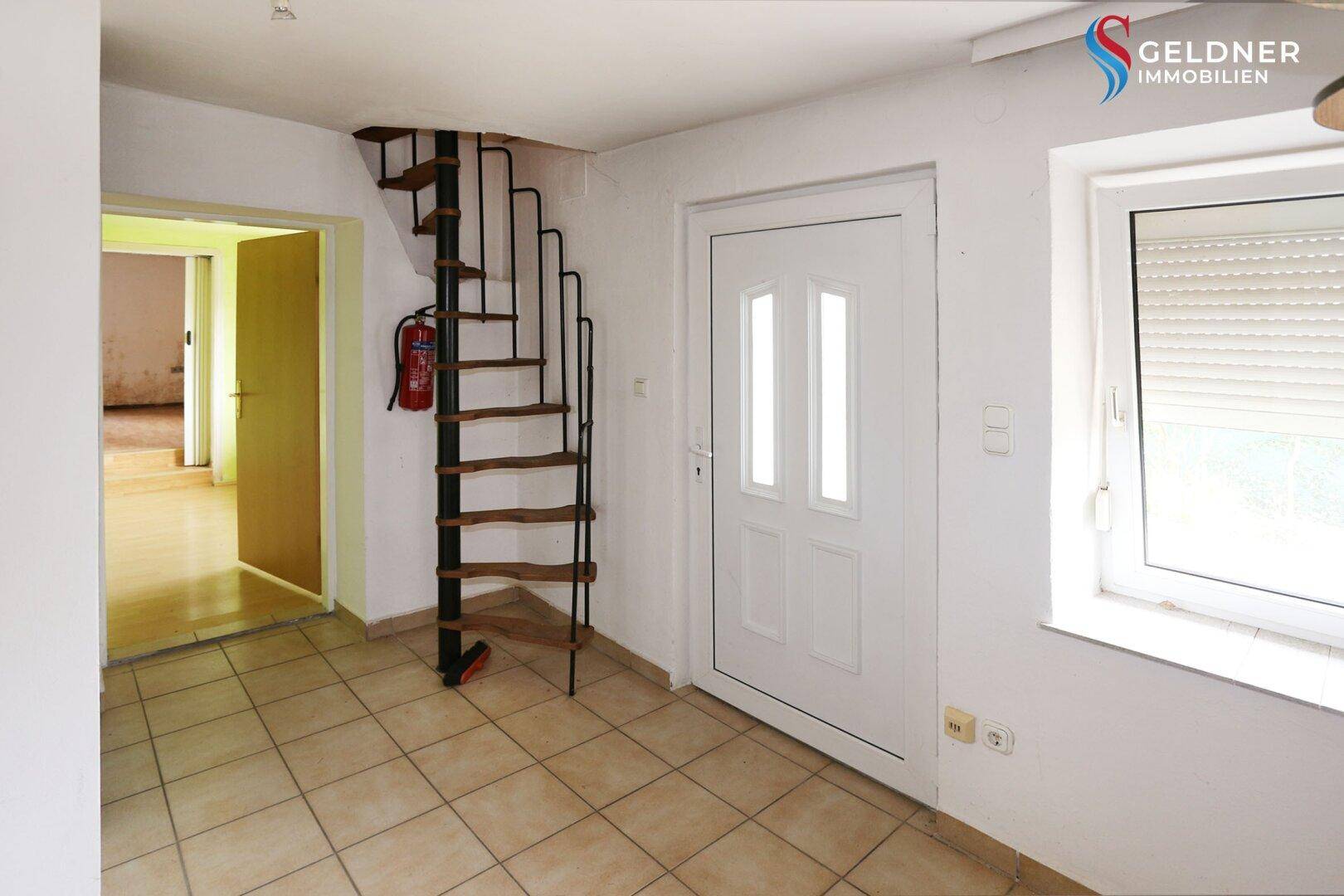 Eingangsbereich mit Fliesenboden, Wendeltreppe und weißer Eingangstür.