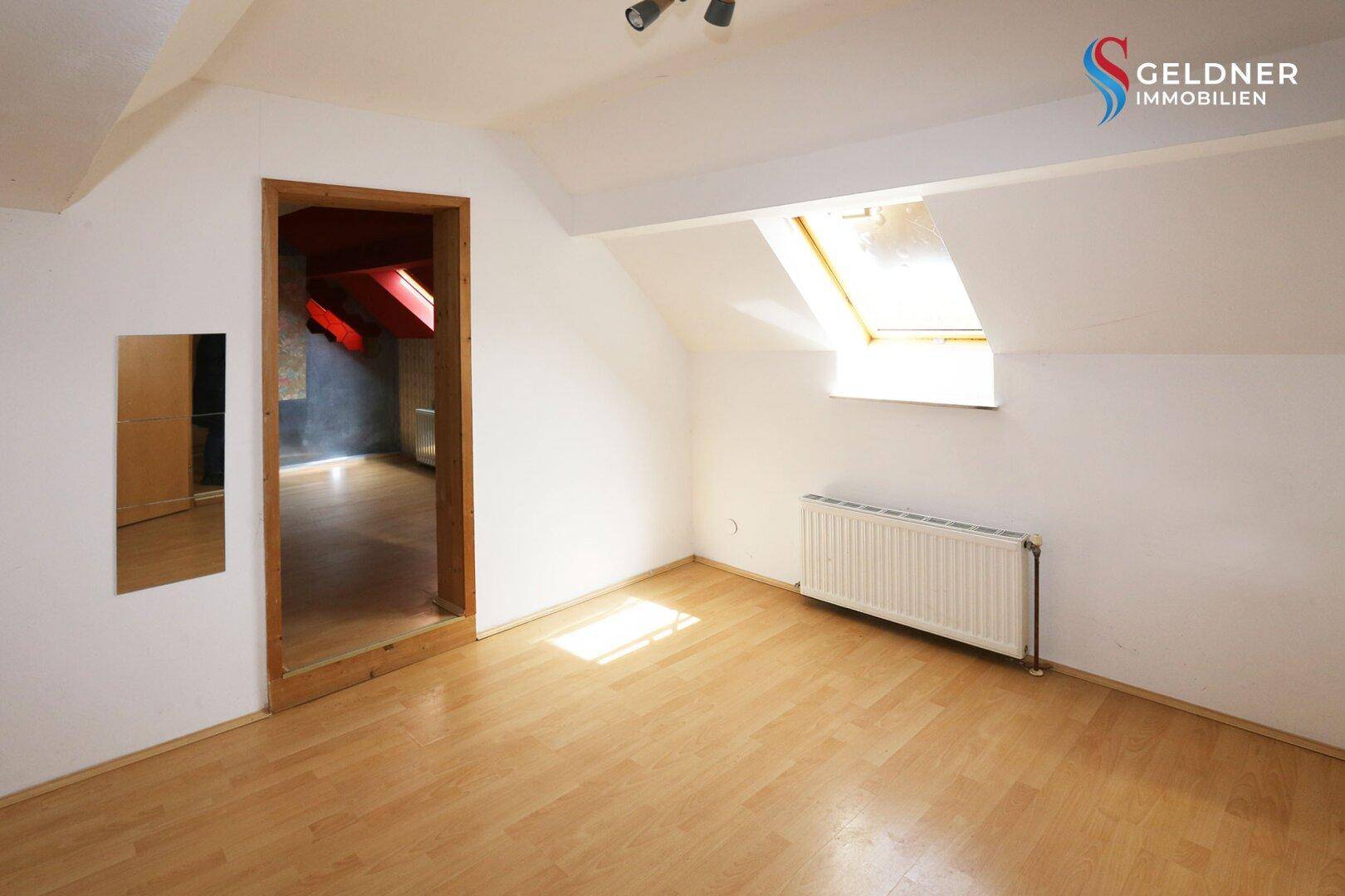 Helles Dachgeschosszimmer mit Laminatboden, Dachfenster und Zugang zu einem weiteren Raum.