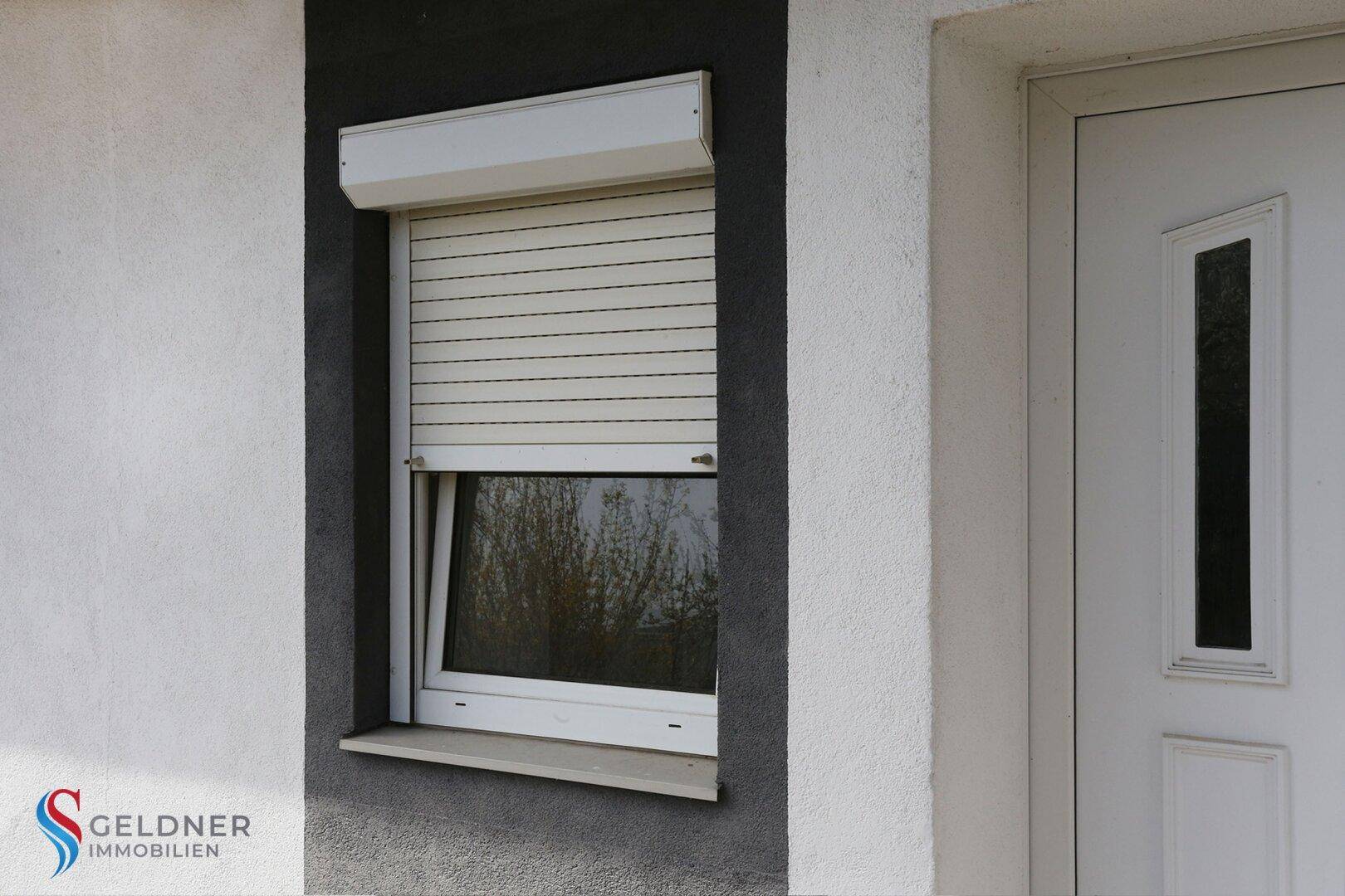 Detailansicht eines Fensters mit Rollladen und der Eingangstür des Hauses.