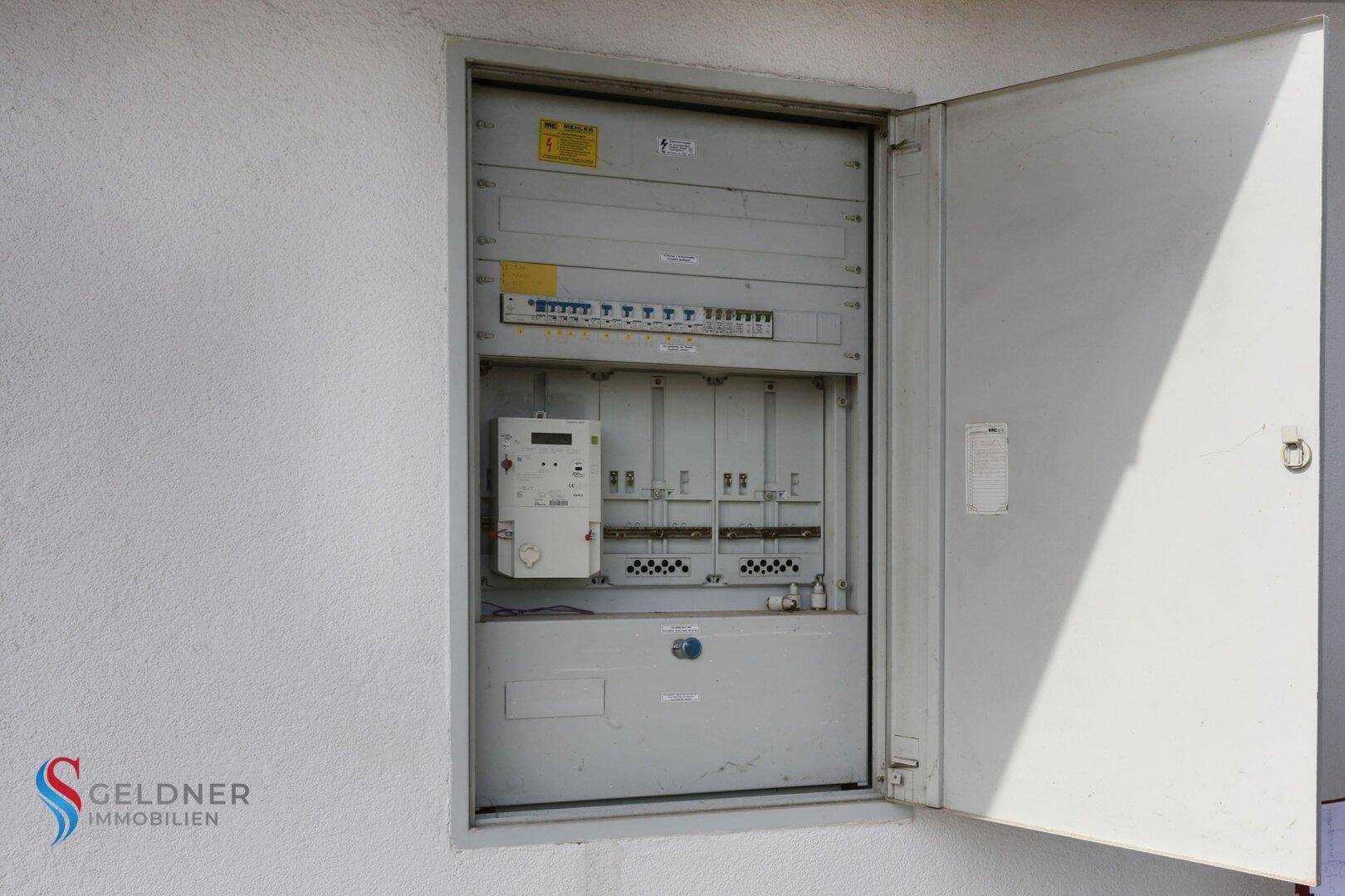 Außenansicht eines geöffneten Sicherungskastens an der Hauswand.