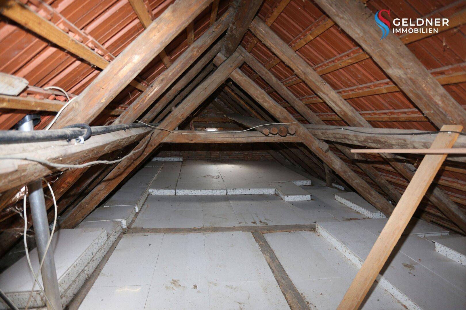 Dachboden mit sichtbarer Holzkonstruktion und Dämmmaterial auf dem Boden.