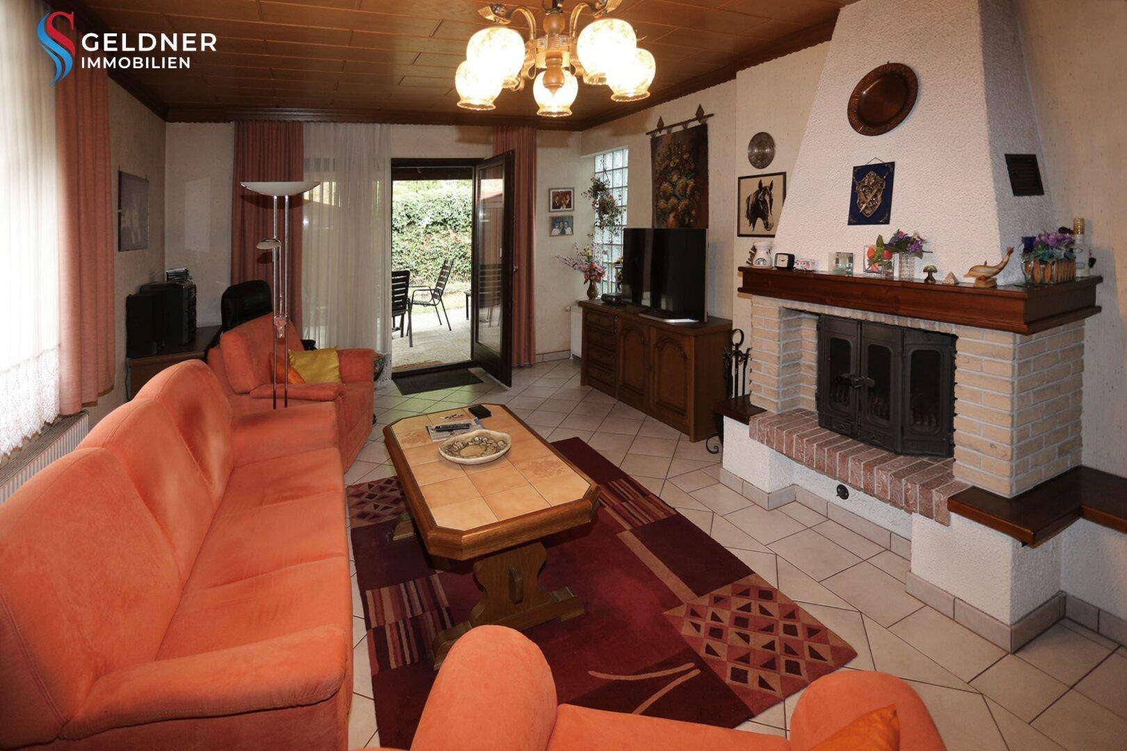 Gemütliches Wohnzimmer mit Kamin, Fliesenboden und Zugang zur Terrasse.