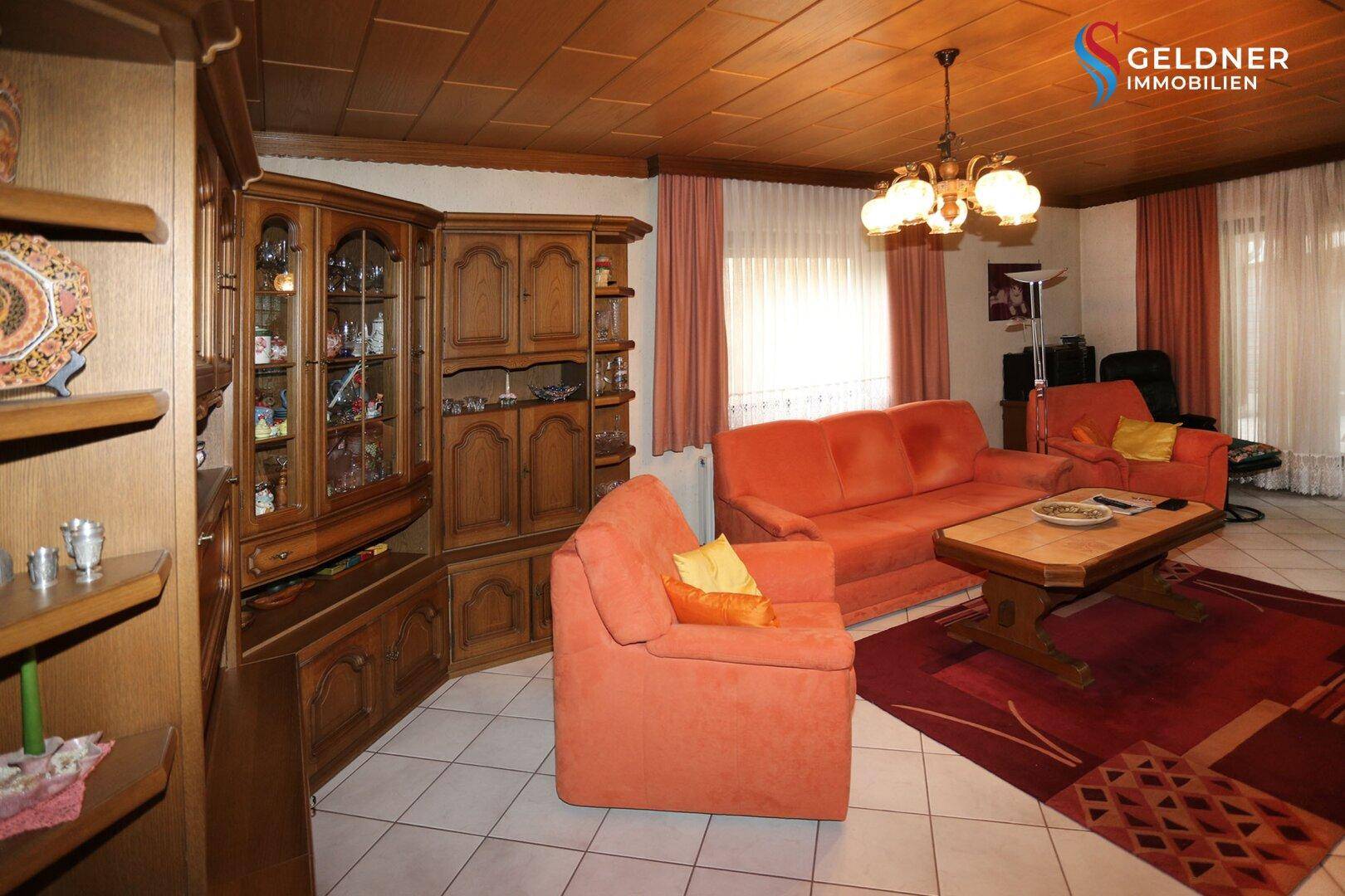 Geräumiges Wohnzimmer mit traditionellen Holzmöbeln, bequemen Sofas und Fliesenboden.