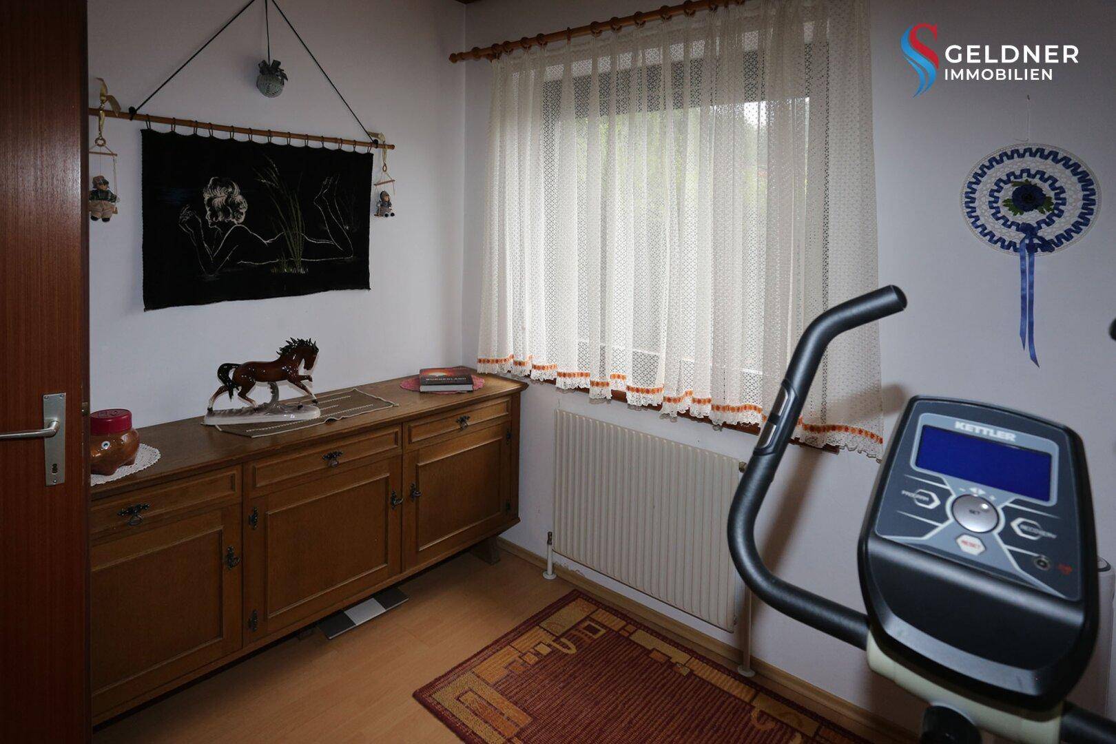 Zimmer mit Schreibtisch, Kommode und Heimtrainer, ideal als Büro oder Hobbyraum.