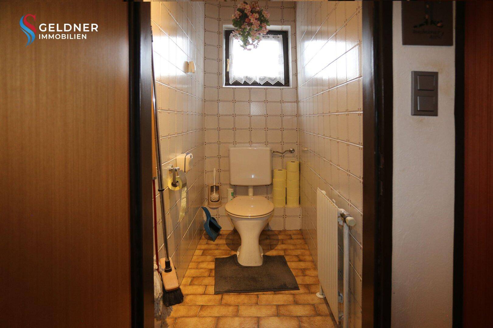 Separate Toilette mit Fenster, gefliesten Wänden und Boden.