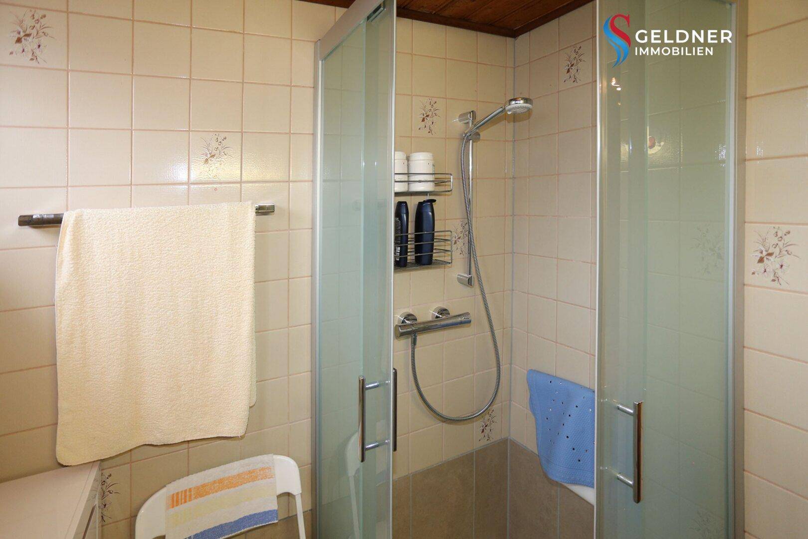 Badezimmer mit Duschkabine und hellen Fliesen, in gutem Zustand.