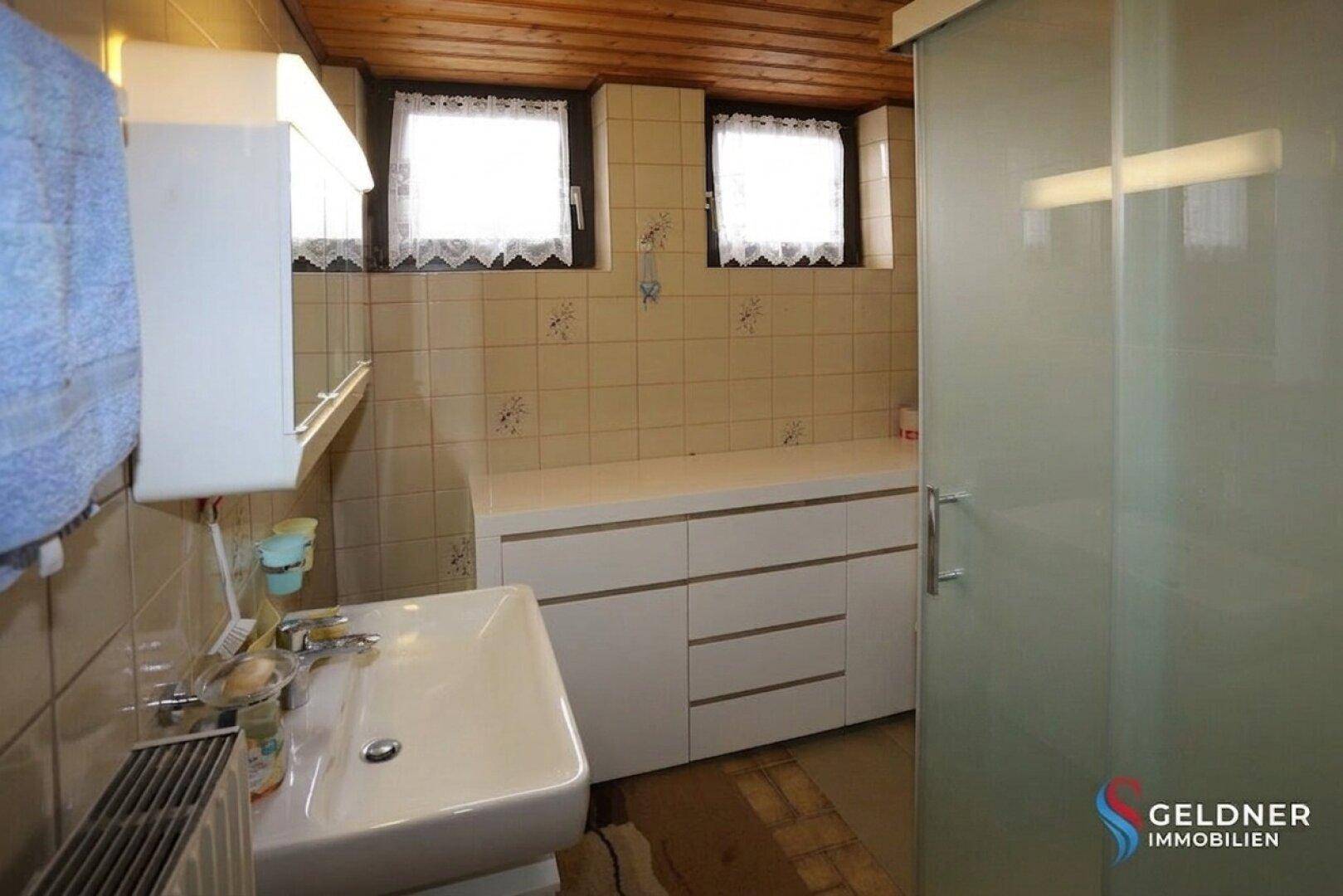 Badezimmer mit Waschbecken, Unterschrank und kleinen Fenstern für Tageslicht.