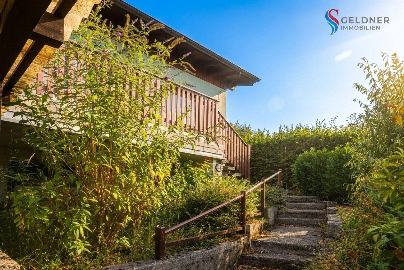 Steintreppe führt durch üppiges Grün zum Eingangsbereich des Hauses.