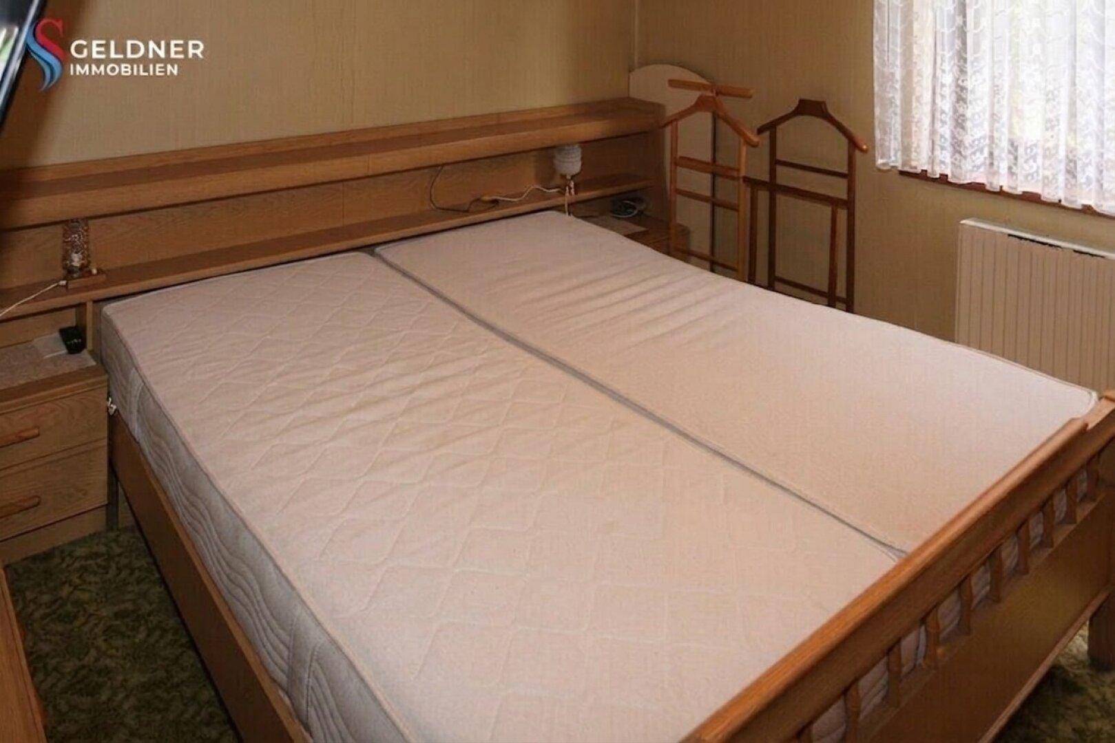 Schlafzimmer mit Doppelbett und Holzrahmen, einfacher Einrichtung.