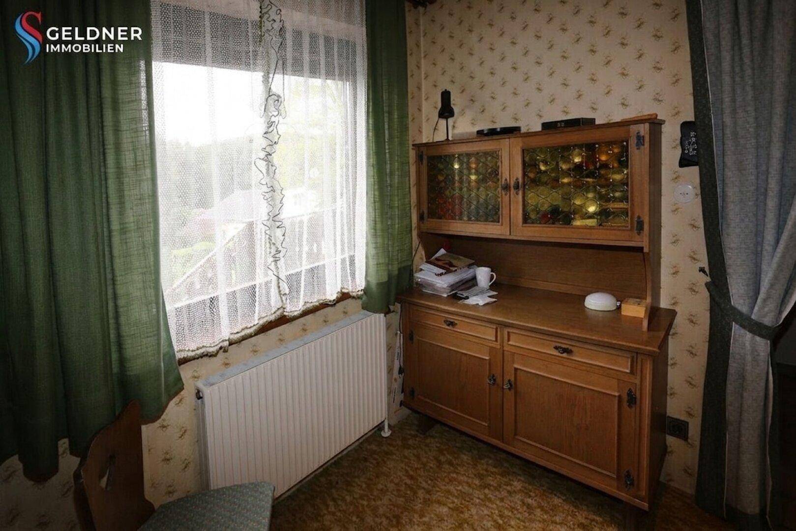 Kleines Zimmer mit Fenster, Holzschrank und einfacher Einrichtung.