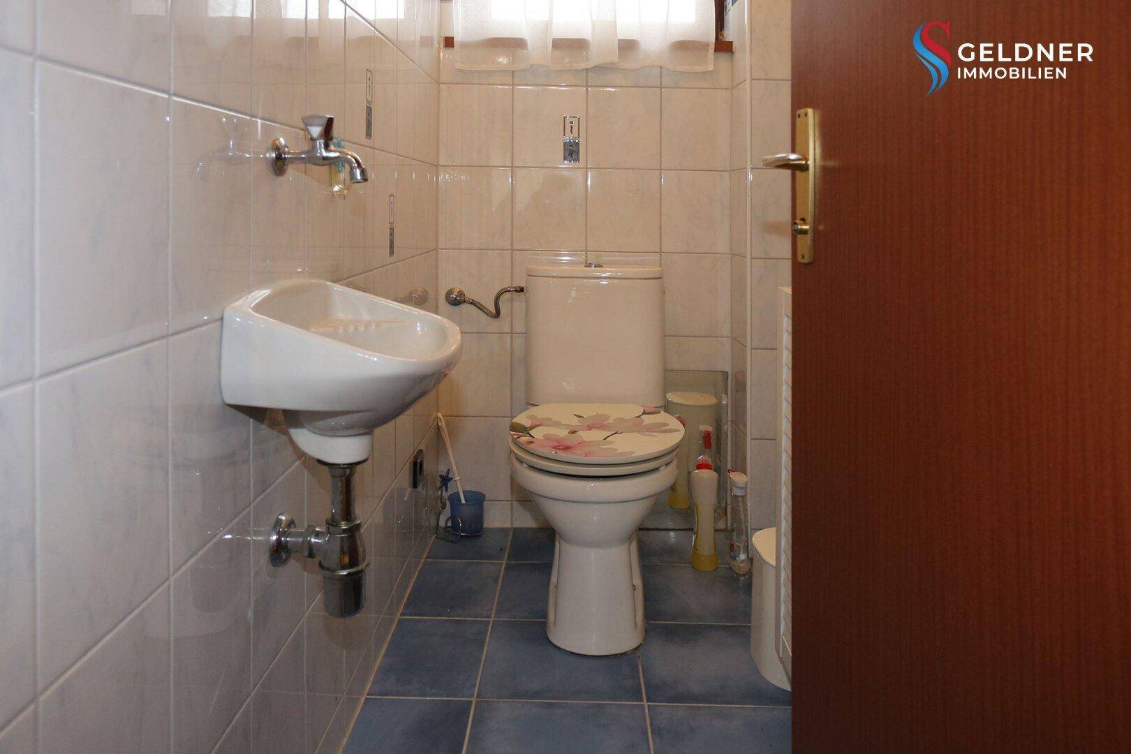 Kleines Gäste-WC mit Wandfliesen, einem Waschbecken und einer Toilette in hellem Ambiente.