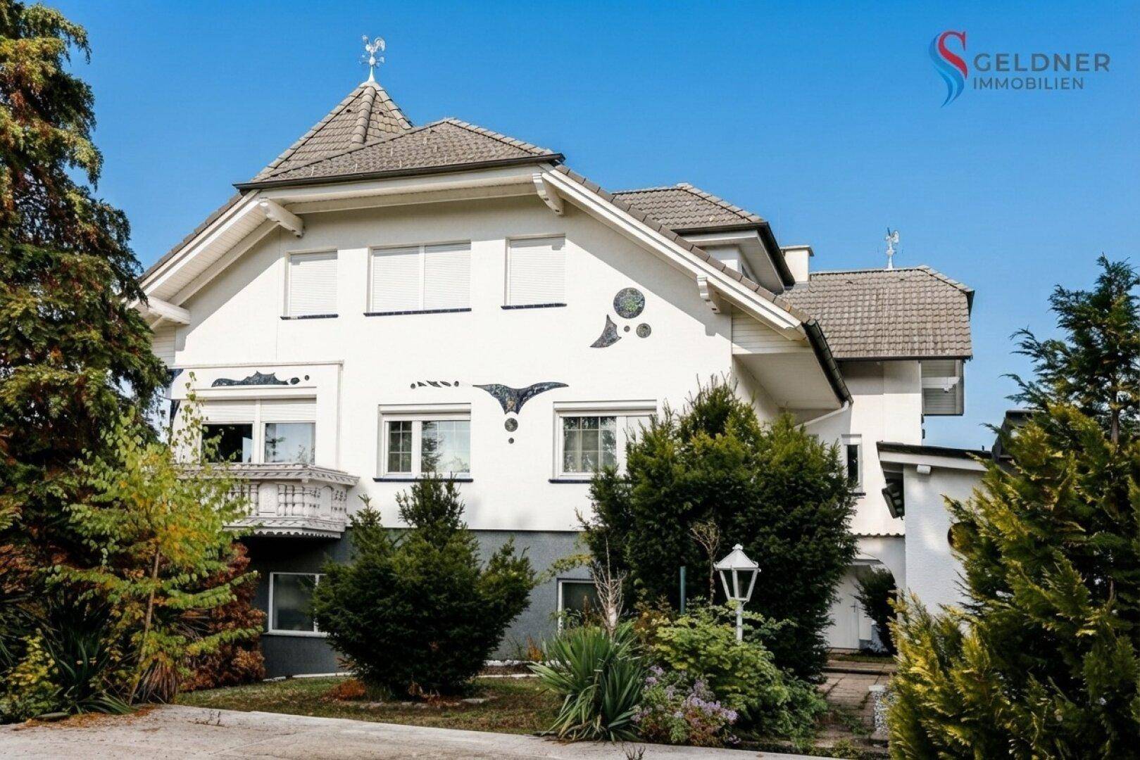Hausfassade von der Gartenseite mit Balkon und üppiger, gepflegter Bepflanzung im Vorgarten.