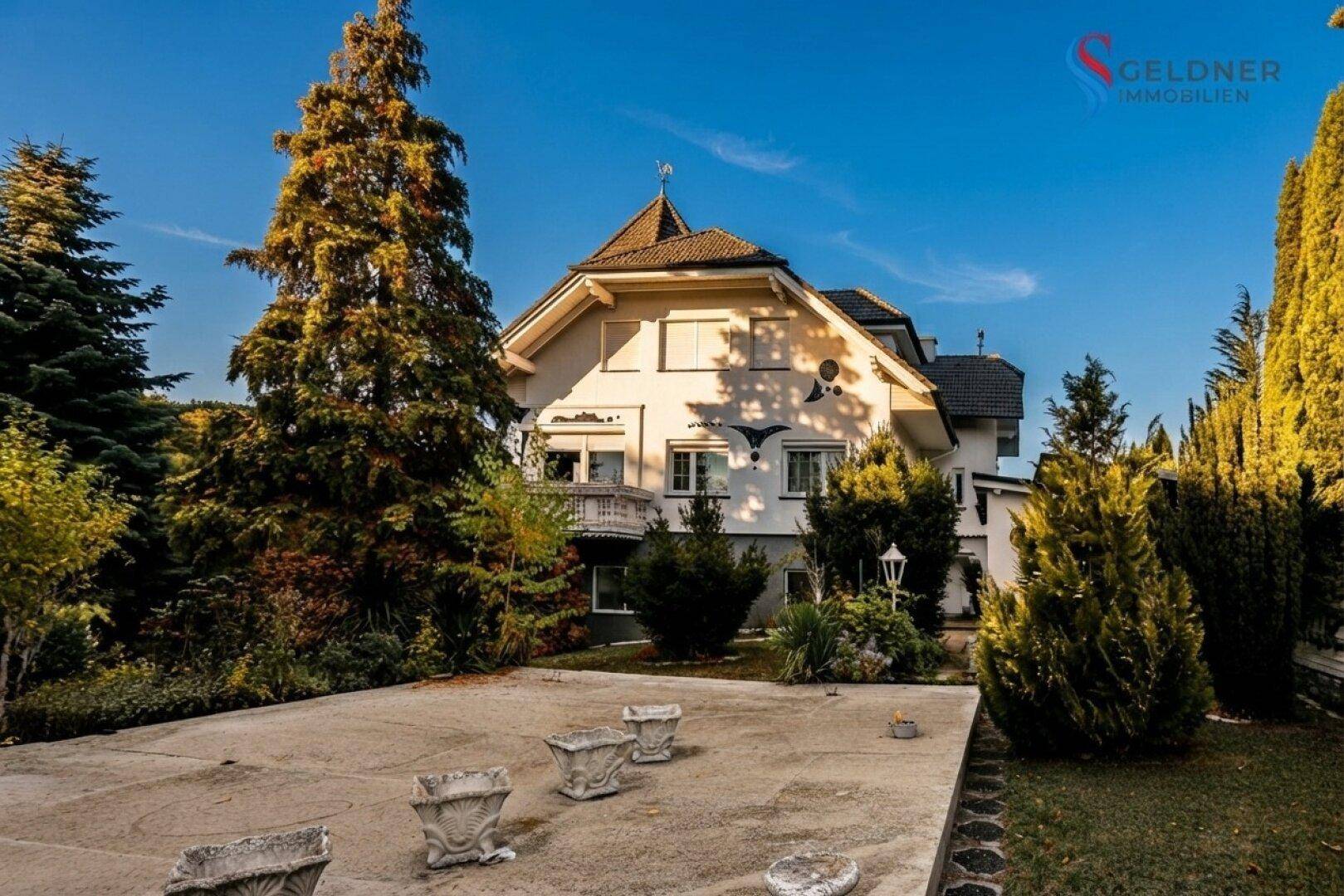 Rückansicht des Hauses mit großem Gartenbereich und alten Bäumen im herbstlichen Sonnenlicht.