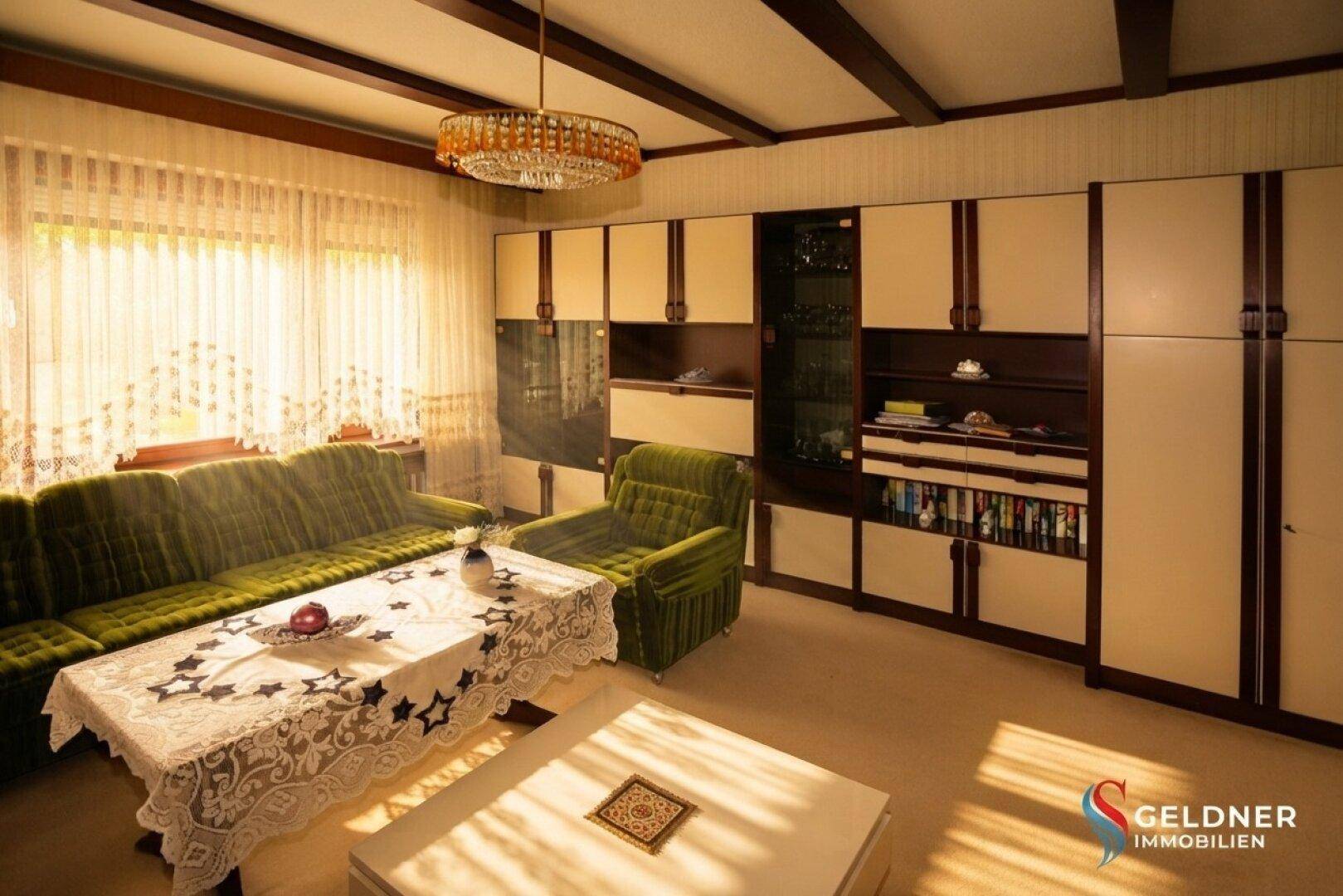 Wohnzimmer mit grünen Sitzmöbeln, großer Schrankwand und heller Fensterfront.