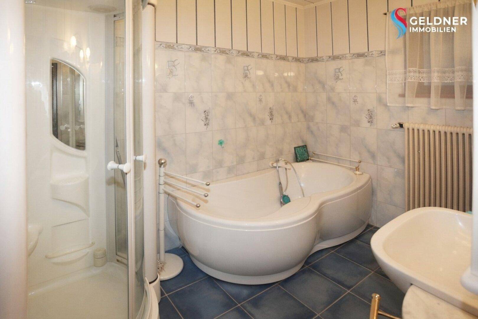 Geräumiges Badezimmer mit einer großen Doppelbadewanne, Duschkabine und blauen Bodenfliesen.