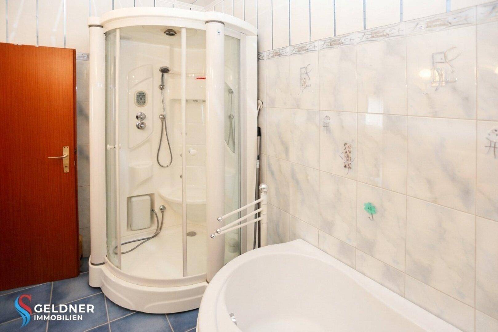 Badezimmer mit einer Duschkabine und einer Badewanne, gefliest in hellen Tönen und blauen Akzenten.