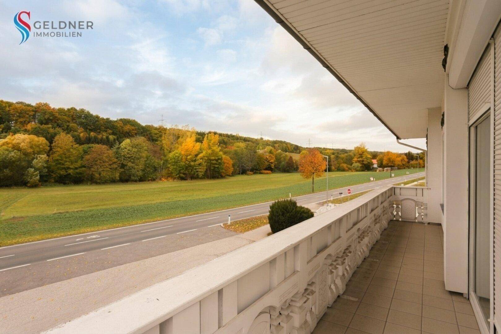 Balkon mit Fliesenboden und weitem Blick auf die grüne Landschaft und eine Landstraße.
