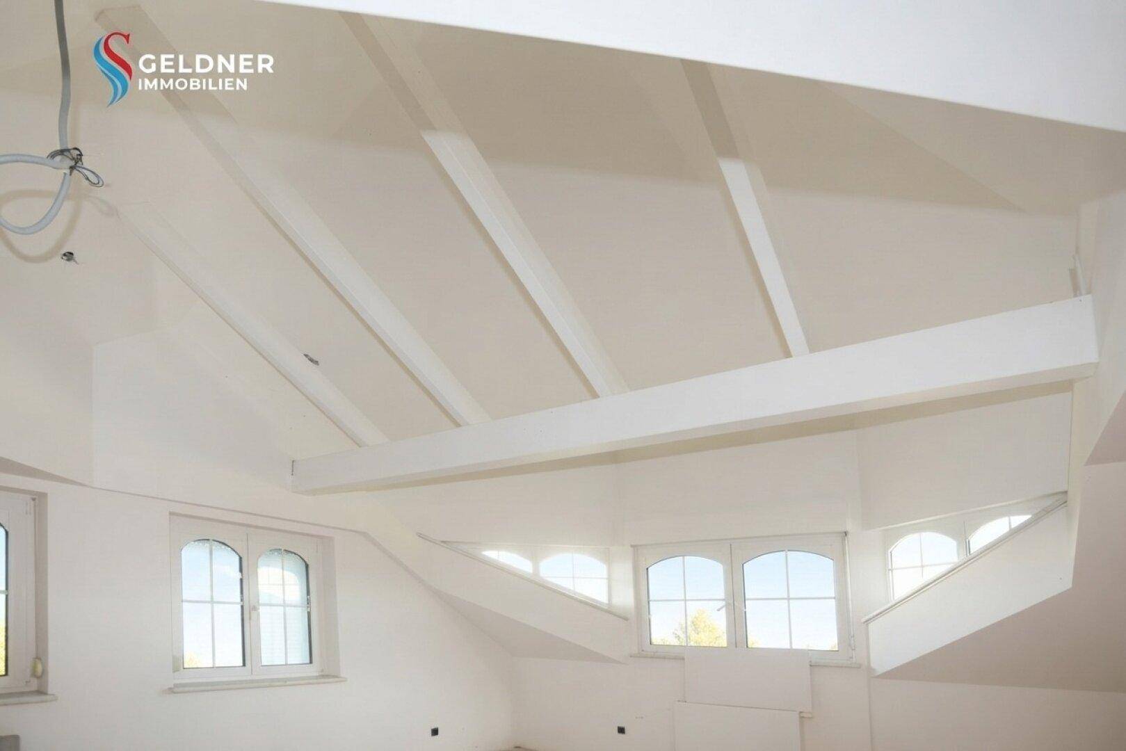Heller Dachbodenraum mit sichtbaren Deckenbalken und mehreren Fenstern, bereit zum Ausbau.