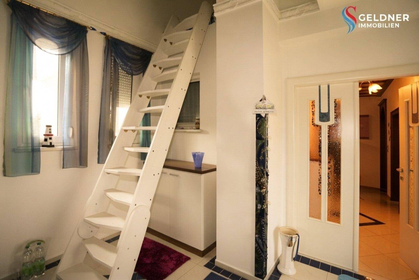 Flur mit einer steilen Holztreppe, die zu einem oberen Bereich führt, und blauen Bodenfliesen.