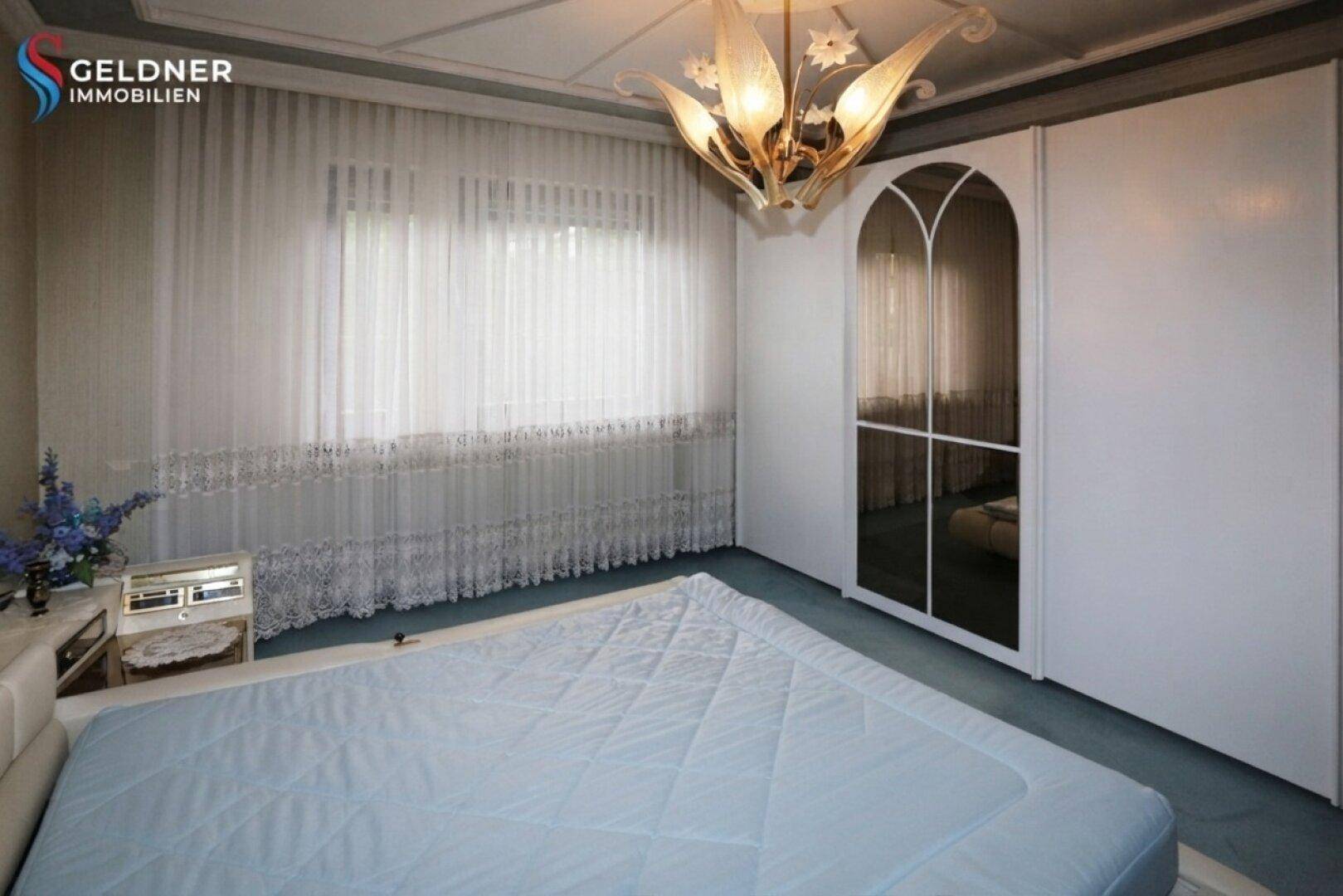 Schlafzimmer mit großem Bett und weißem Kleiderschrank mit Spiegeltür, in einem hellen Ambiente.