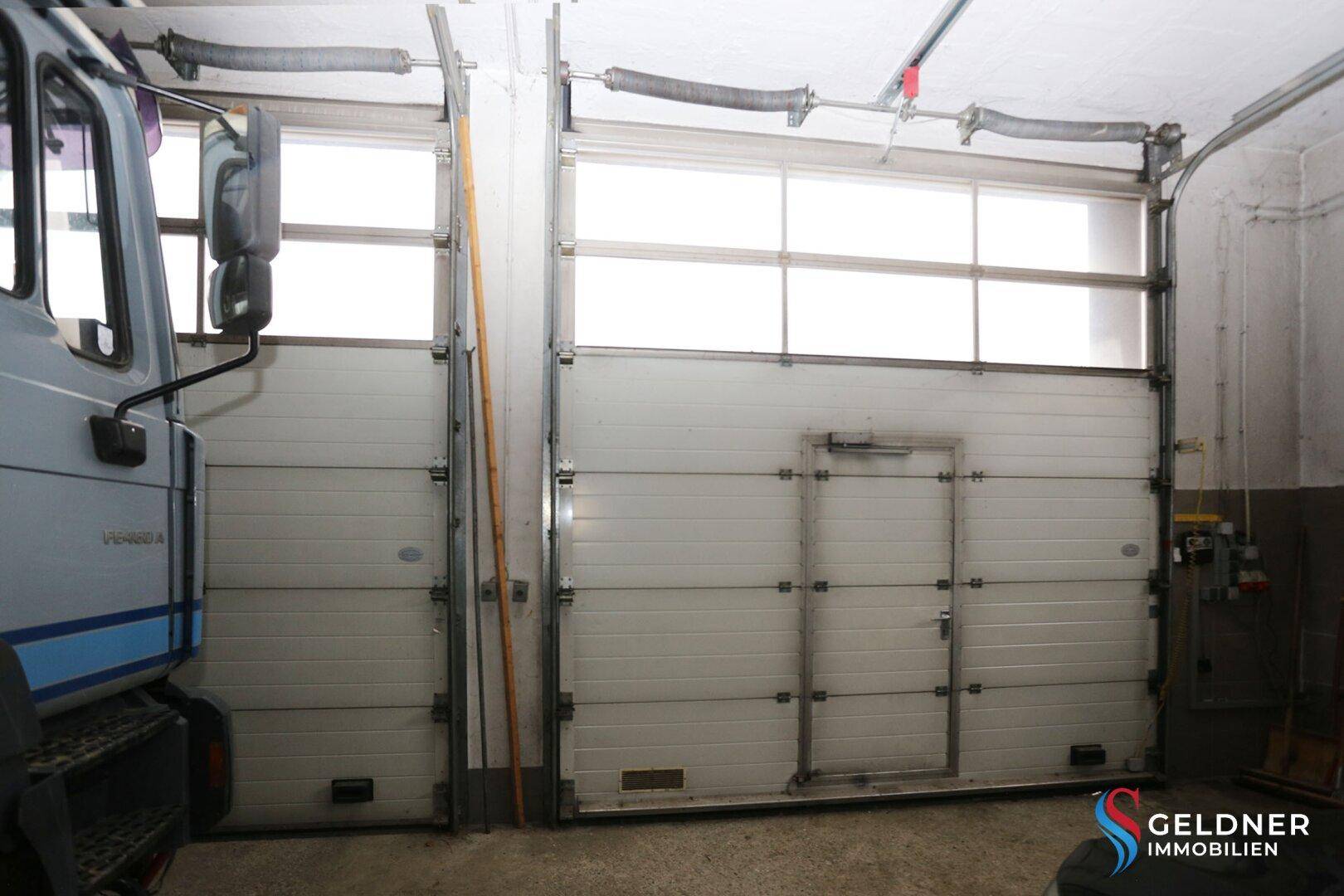 Zwei große Garagentore mit integrierter Tür und oberen Fensterpaneelen für Tageslicht.