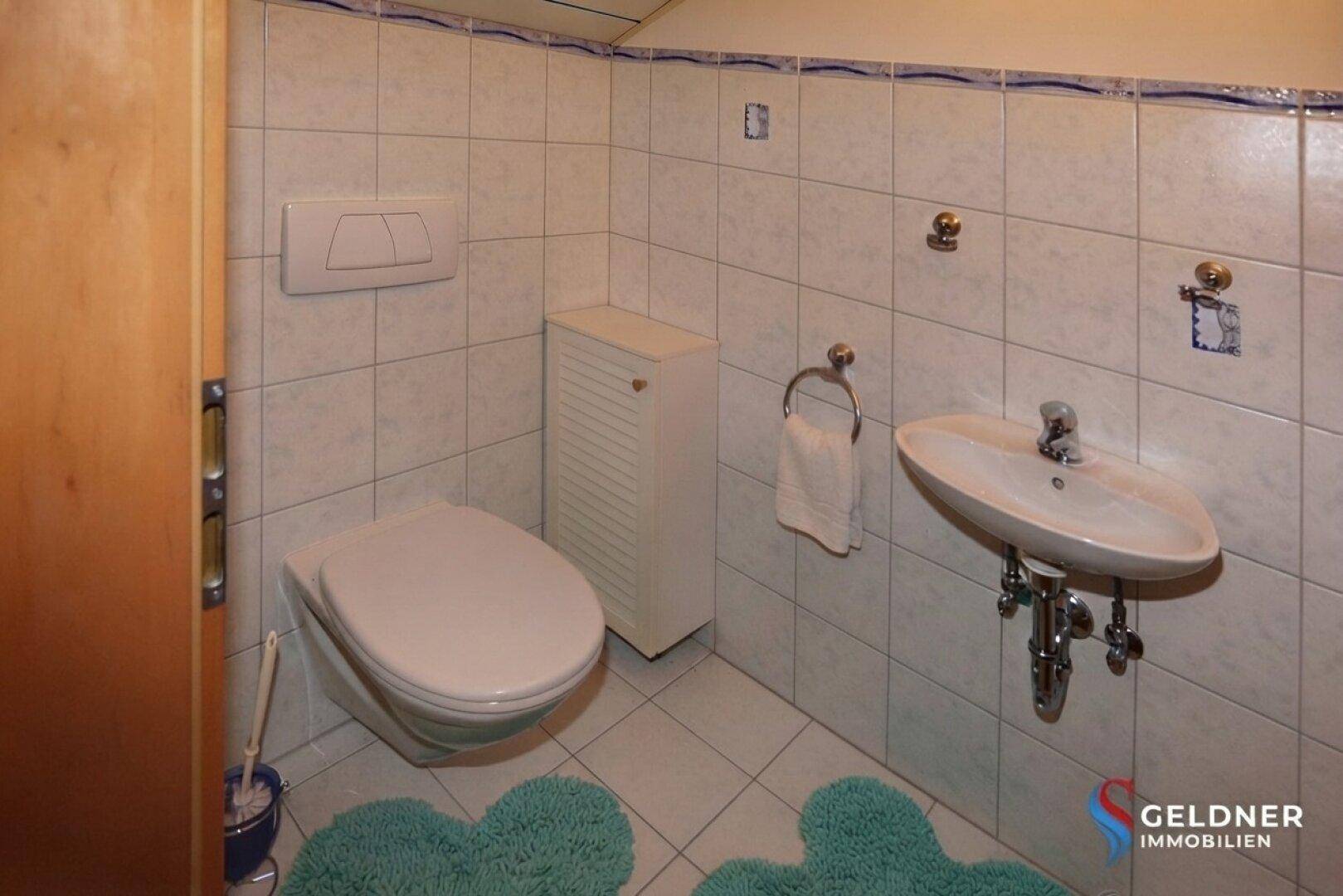 Modernisiertes WC mit Wand-WC, kleinem Waschbecken und hellen Fliesen in gutem Zustand.