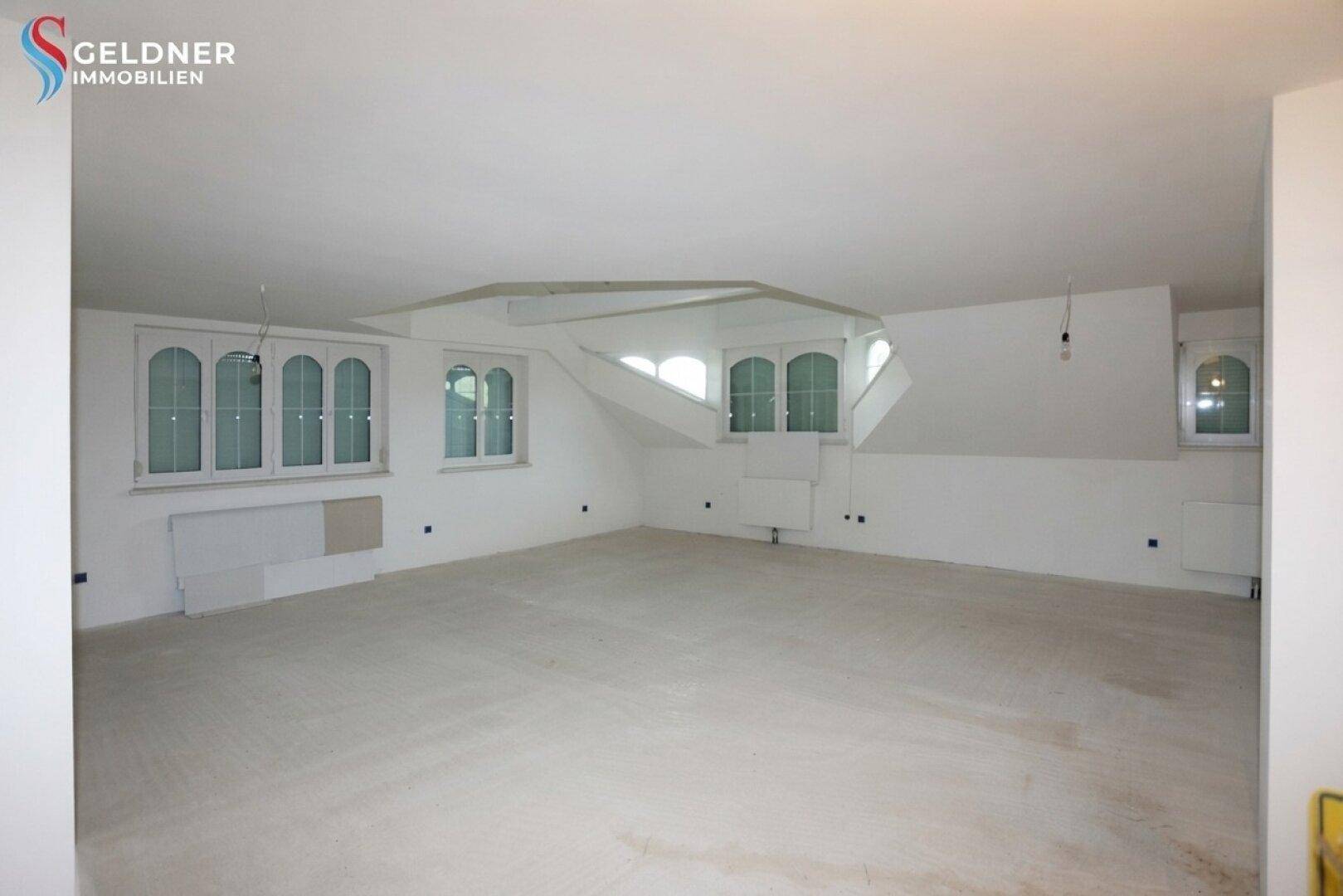 Großer, heller Dachbodenraum mit mehreren Fenstern und schrägen Wänden, bereit zum Ausbau.