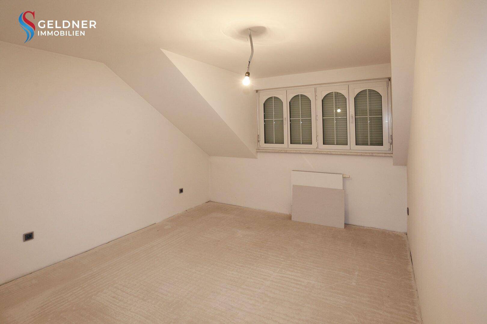 Dachbodenraum mit schrägen Wänden und einem Fenster, bereit für den Innenausbau und neue Nutzung.