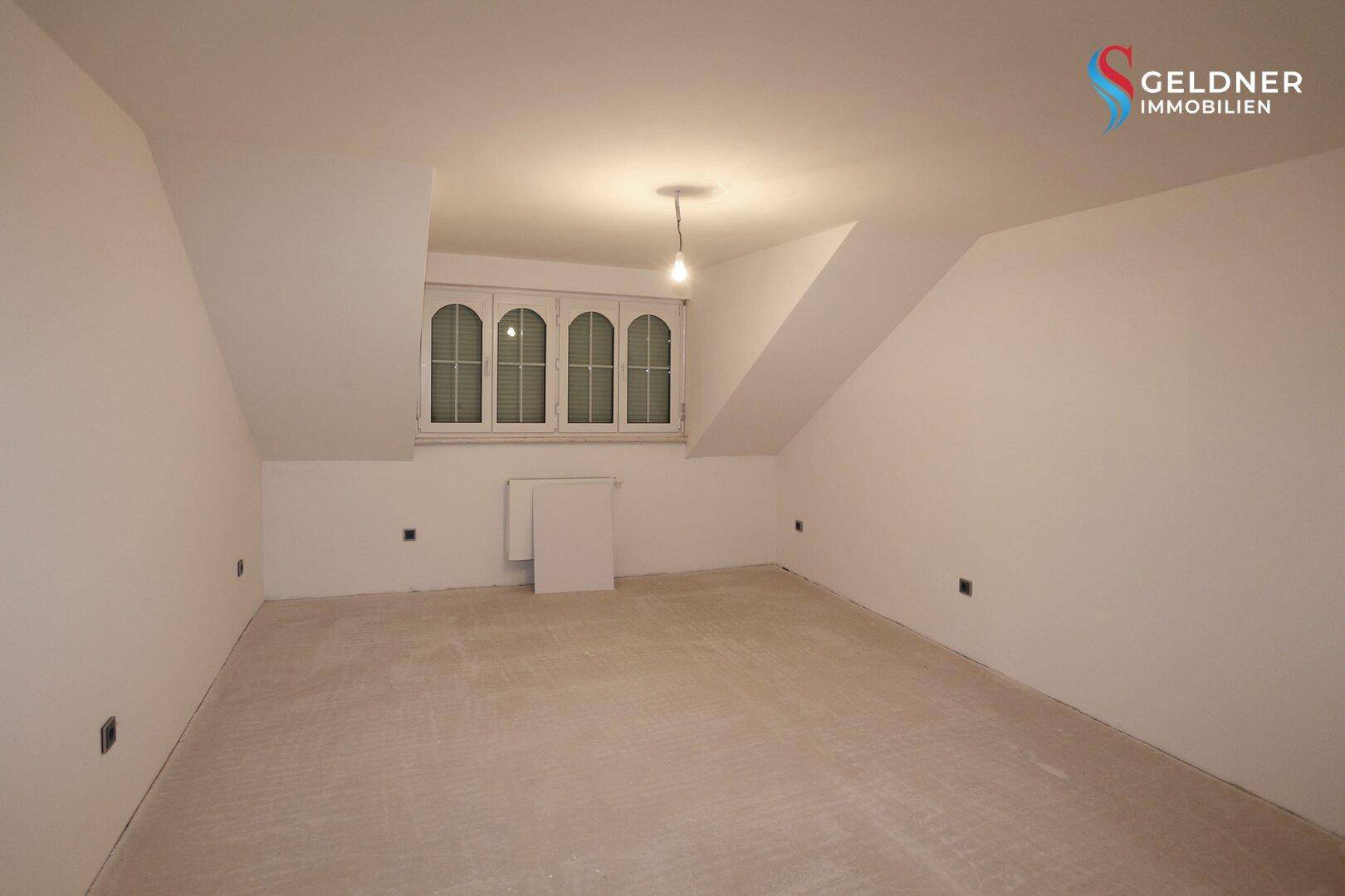 Dachbodenraum mit schrägen Wänden und einem Fenster, ideal für ein Schlafzimmer oder Büro.