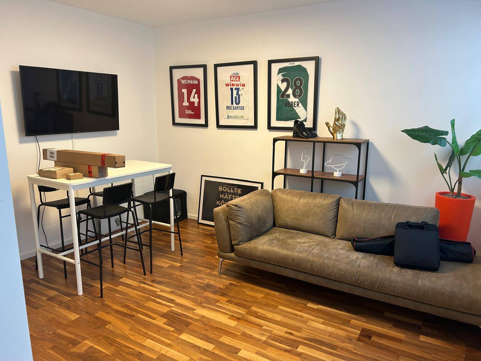 Gemütlicher Loungebereich mit Sofa, Stehtisch und Fernseher, ideal für Pausen oder informelle Treffen.