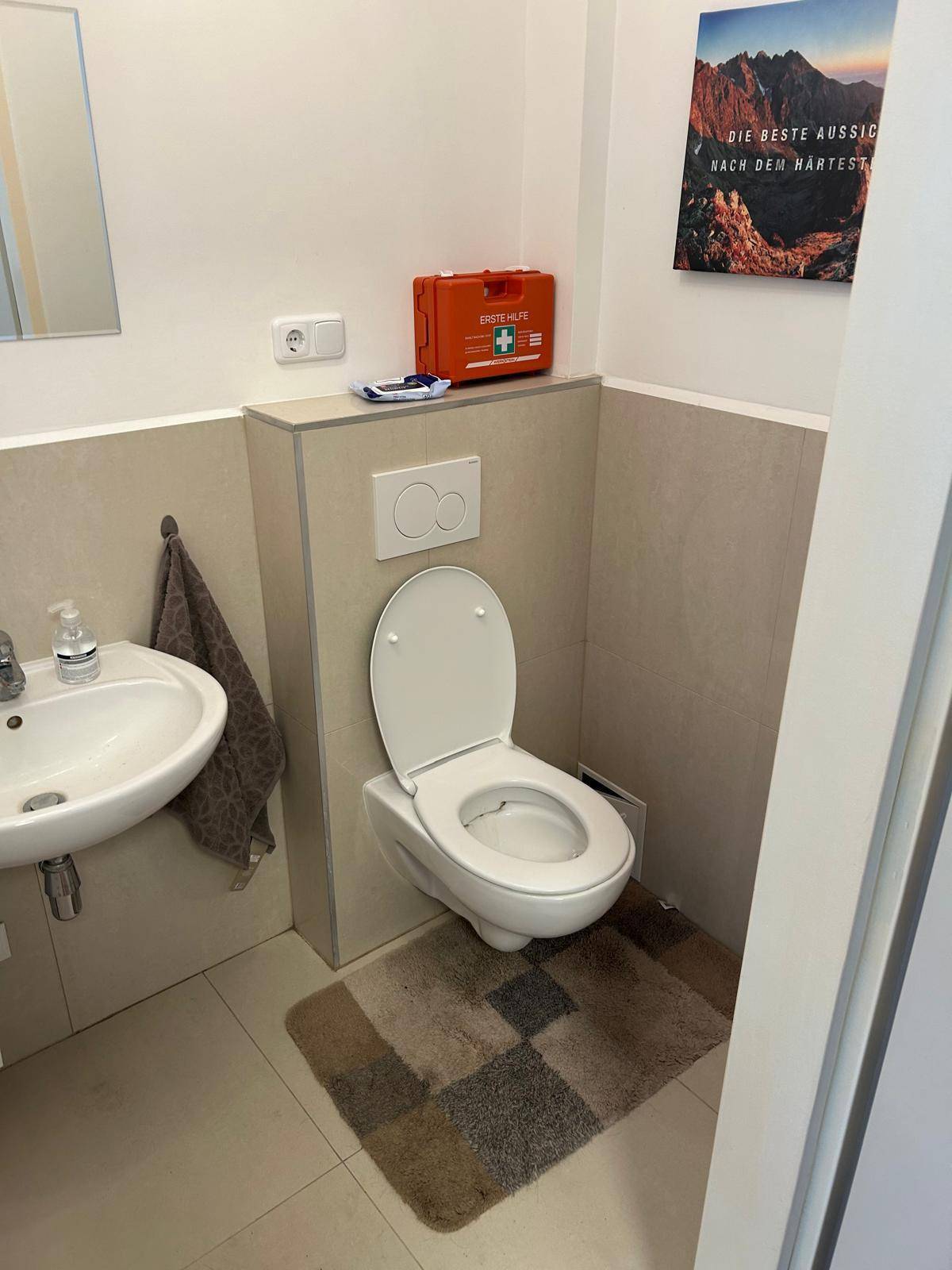 Separate Toilette mit wandhängendem WC, Waschbecken und Fliesenboden in modernem Design.