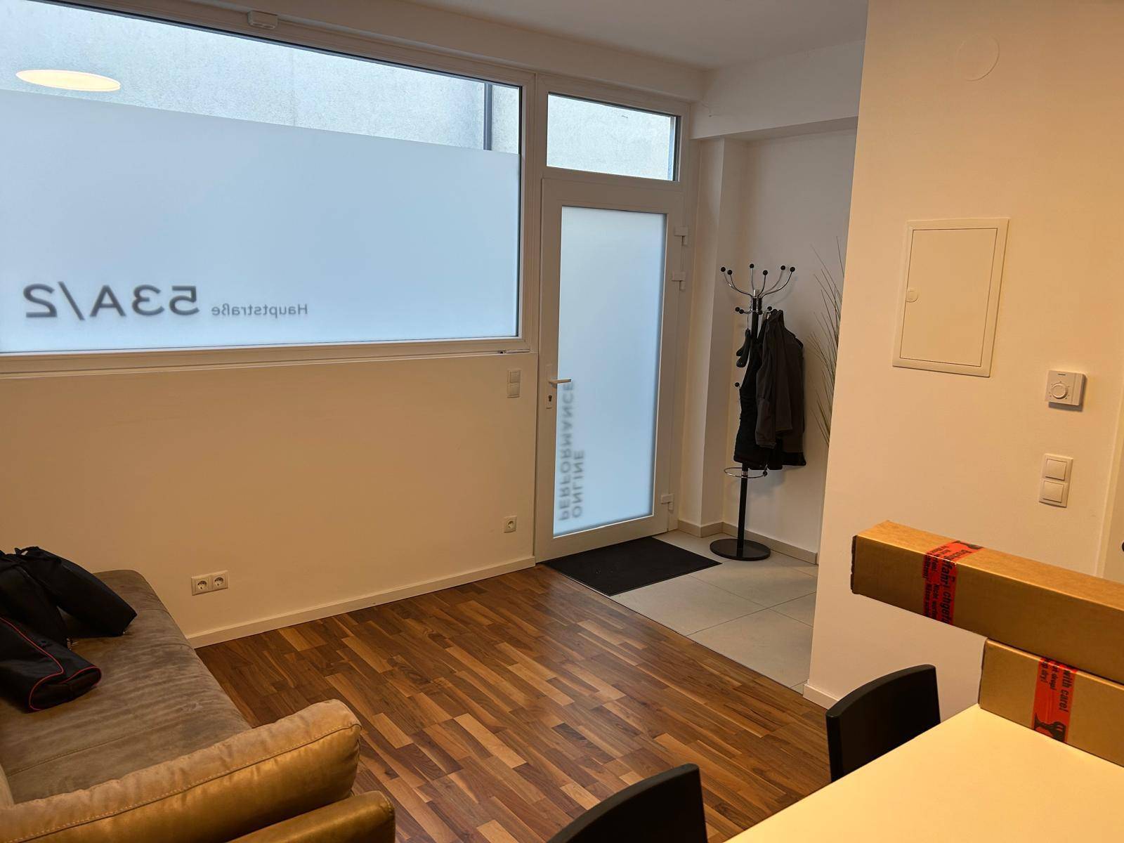 Heller Eingangsbereich mit Holzboden, Garderobe und einer großen Fensterfront mit Milchglasfolie.