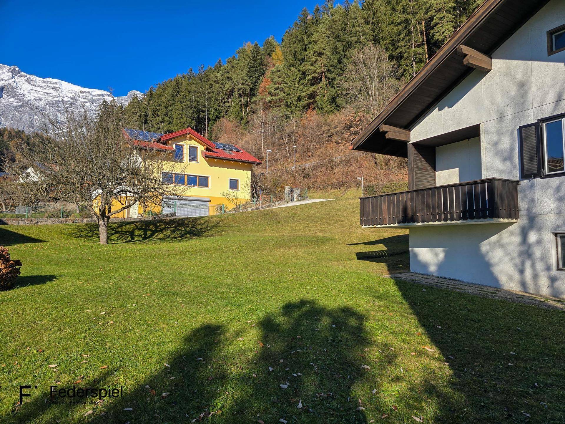 Weitläufiger Garten mit Rasenfläche und Blick auf bewaldete Hügel und schneebedeckte Berge.