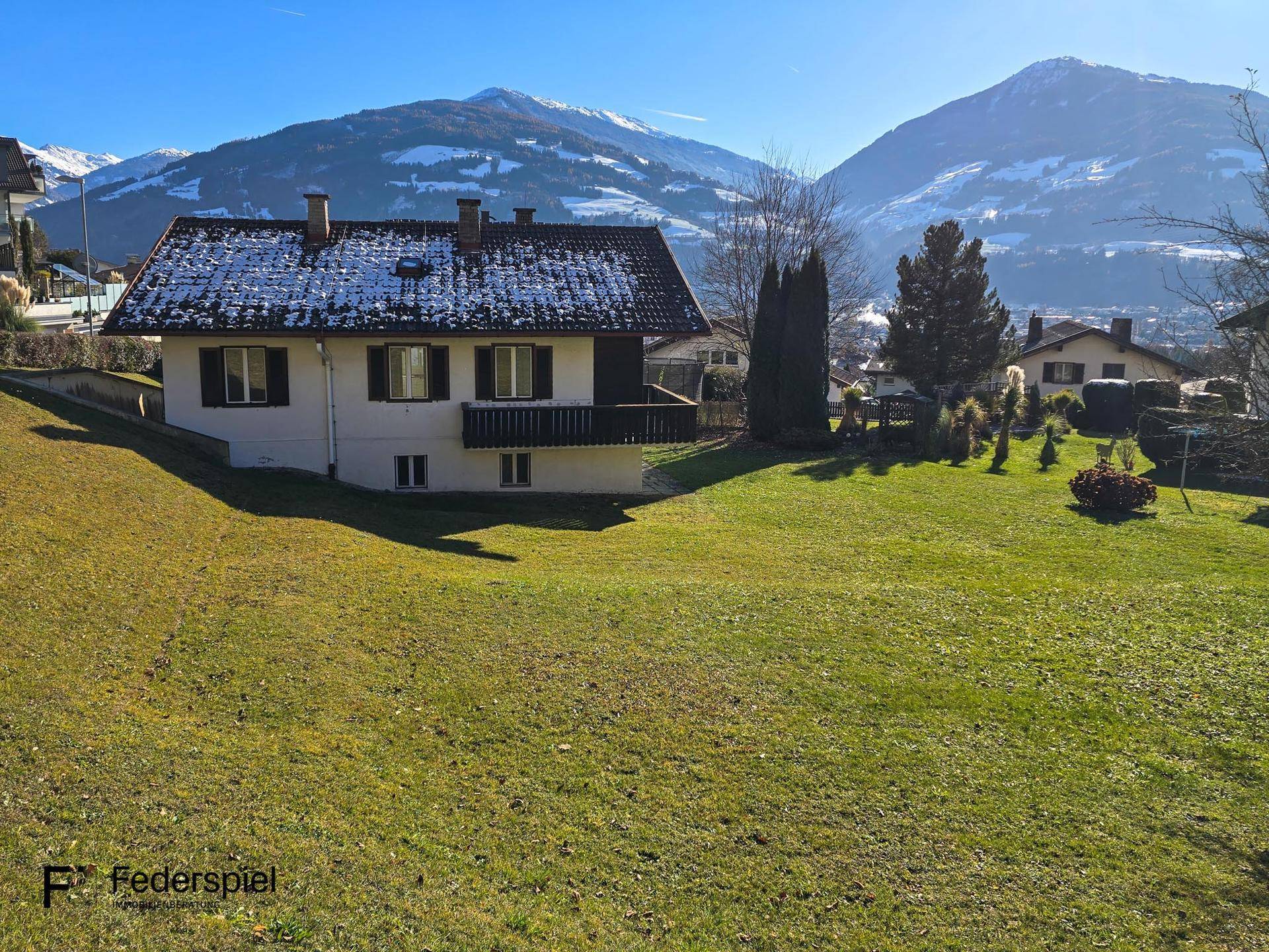 Traditionelles Haus mit schneebedecktem Dach und weitem Blick auf die Berge an einem sonnigen Tag.