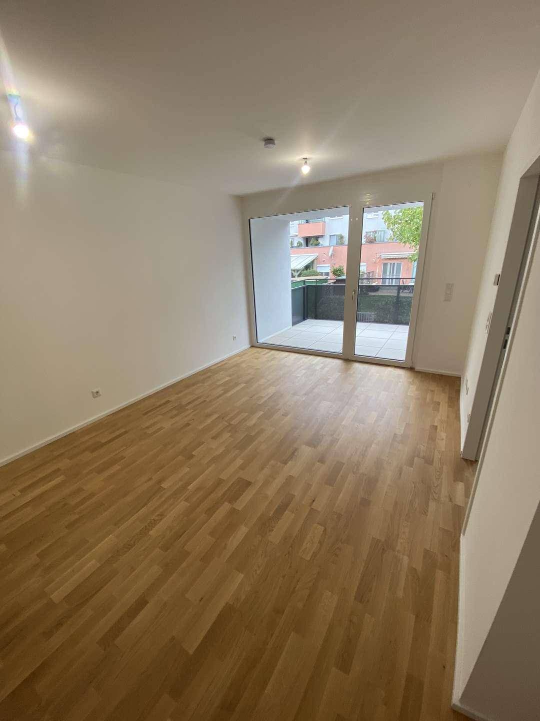 Heller Wohnbereich mit Holzparkett und großen Fenstern, die auf einen modernen Balkon führen.