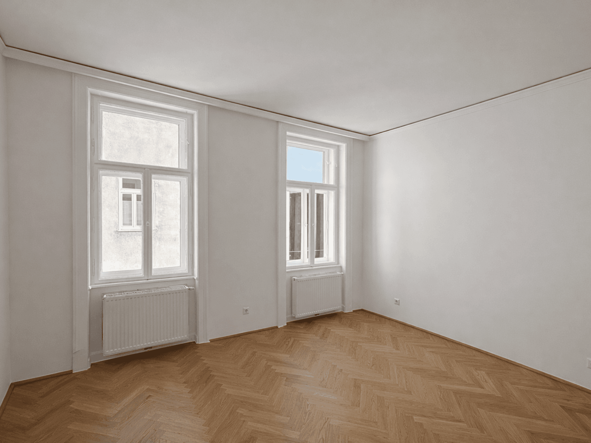 Geräumiges, helles Zimmer mit Fischgrätparkett, hohen Fenstern und Heizkörpern.