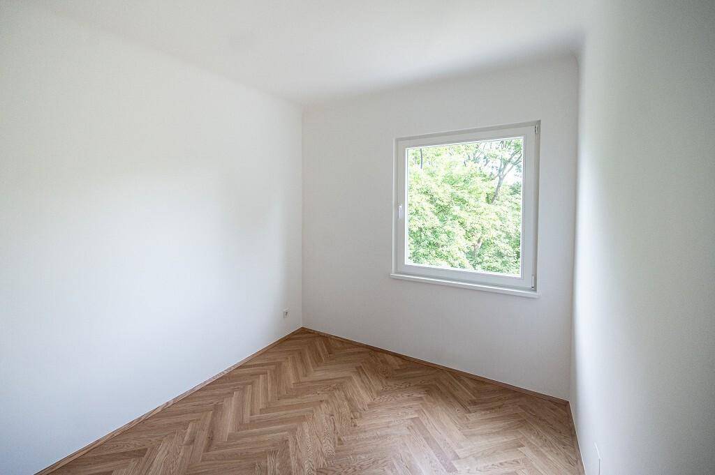 Helles Zimmer mit Fischgrätparkett und einem Fenster mit Blick auf die grüne Umgebung.